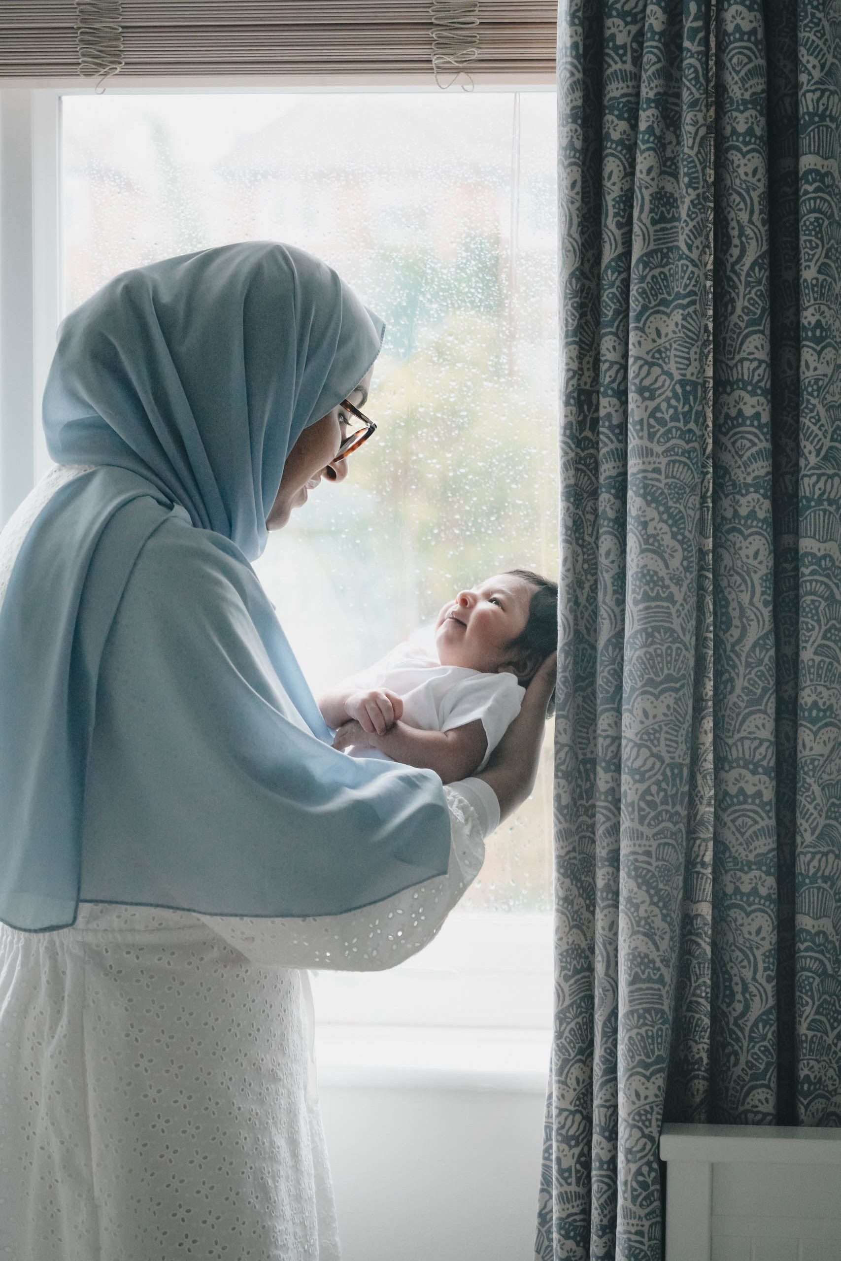 Mother holding newborn baby by the window during a soft natural light newborn photography session in Solihull