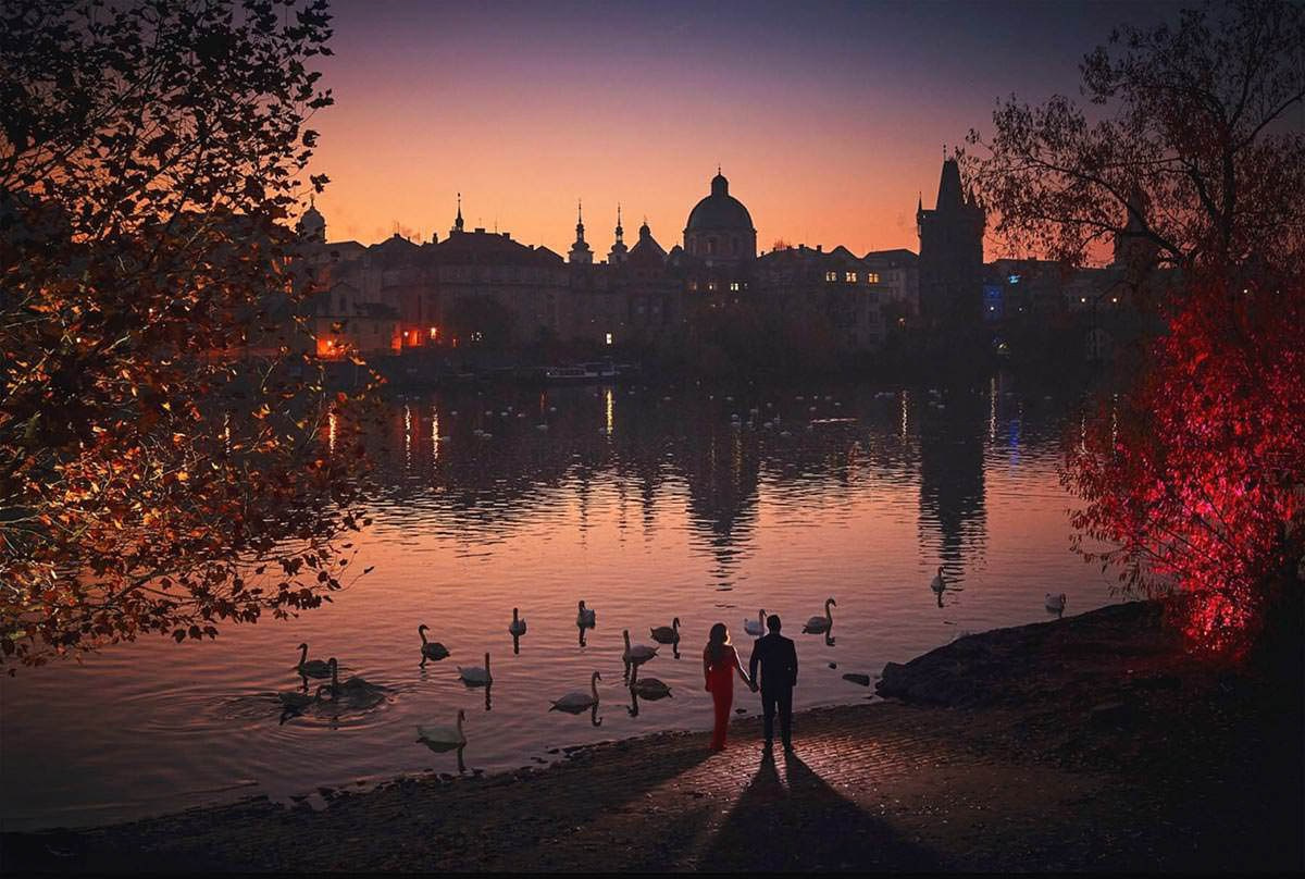 Vltava Riverbanks sunrise engagement in Prague — American couple near Charles Bridge as swans glide by
