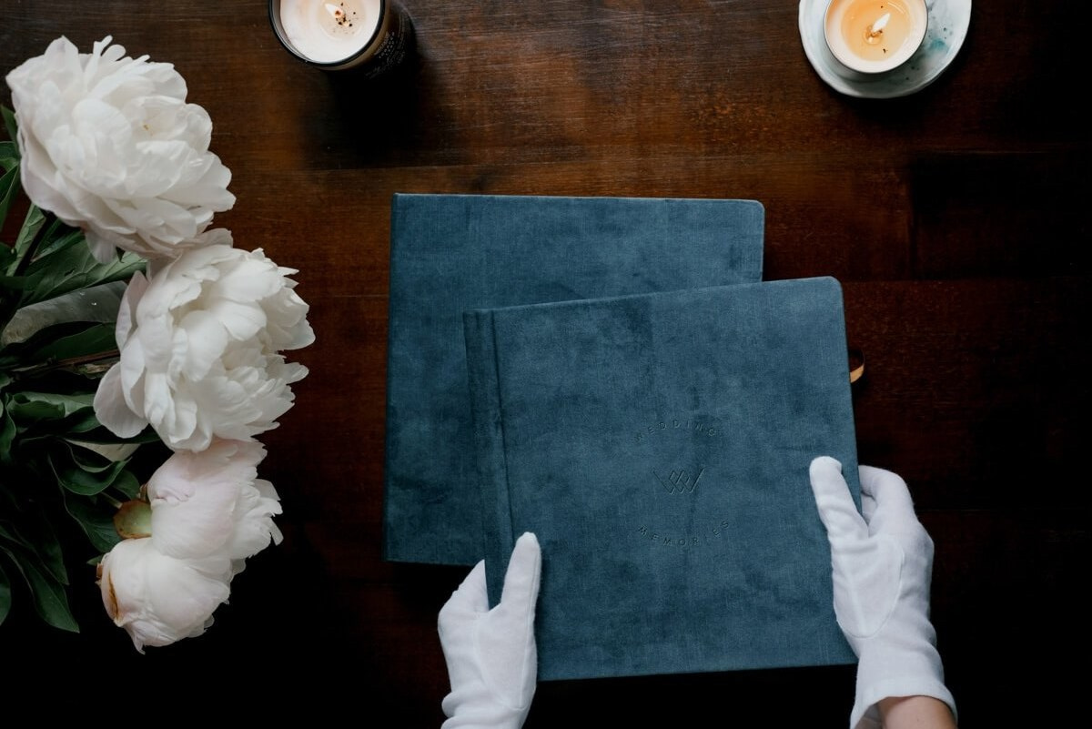 Two fine art wedding albums held with gloves on table