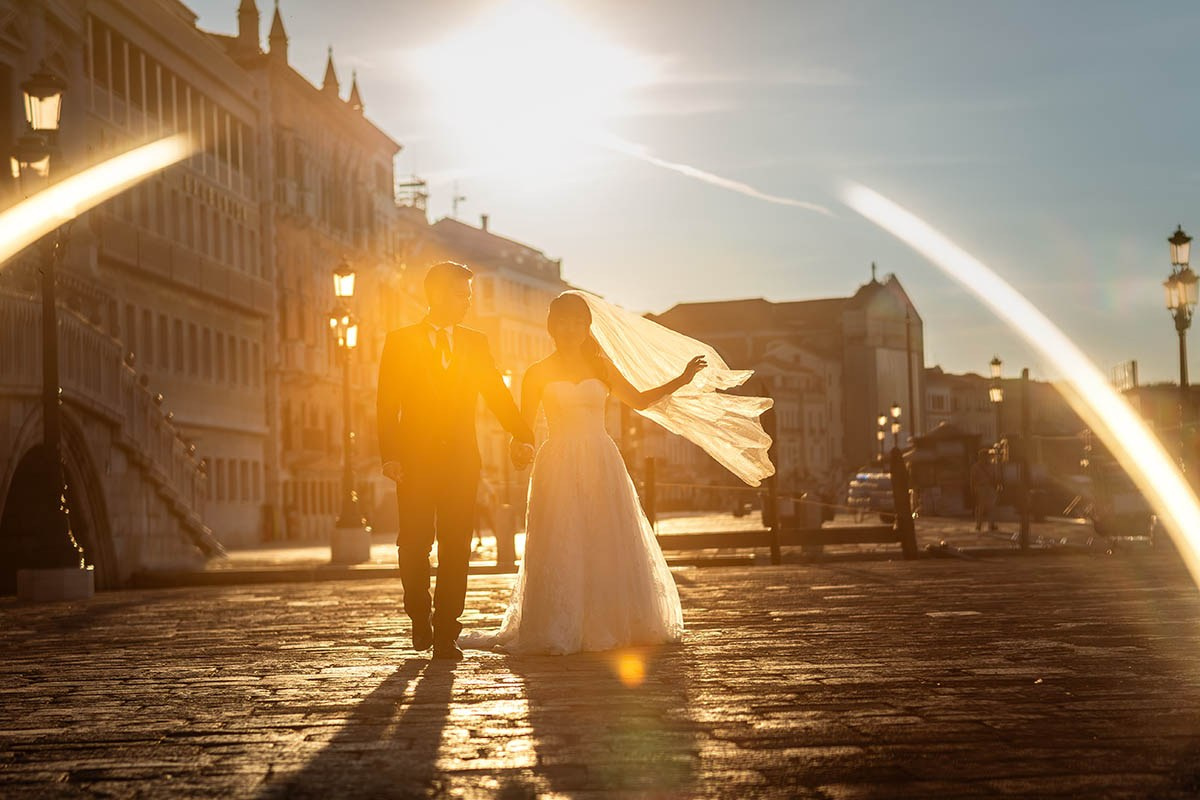 A couple walks alone along the historic canal in Venice, Italy as the sun flares dramatically around them - Kurt Vinion Photography