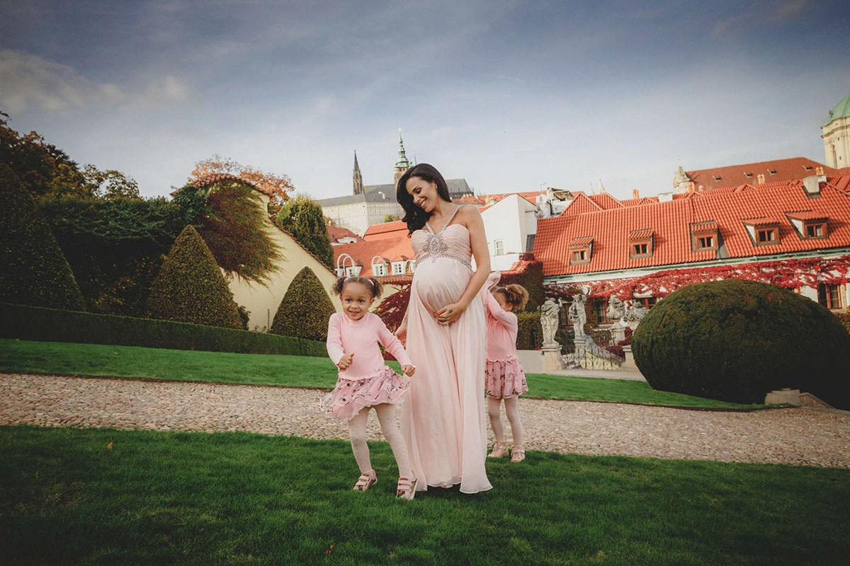 Pregnant mother walking on the lawn at Vrtba Garden as her daughters play around her