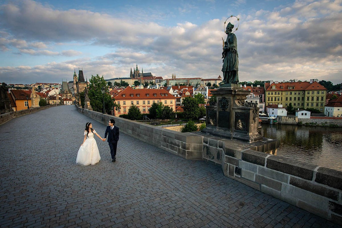 A birds-eye view of Korean newlyweds as they stroll along the empty landscape of the Charles Bridge in Prague shortly after sunrise.