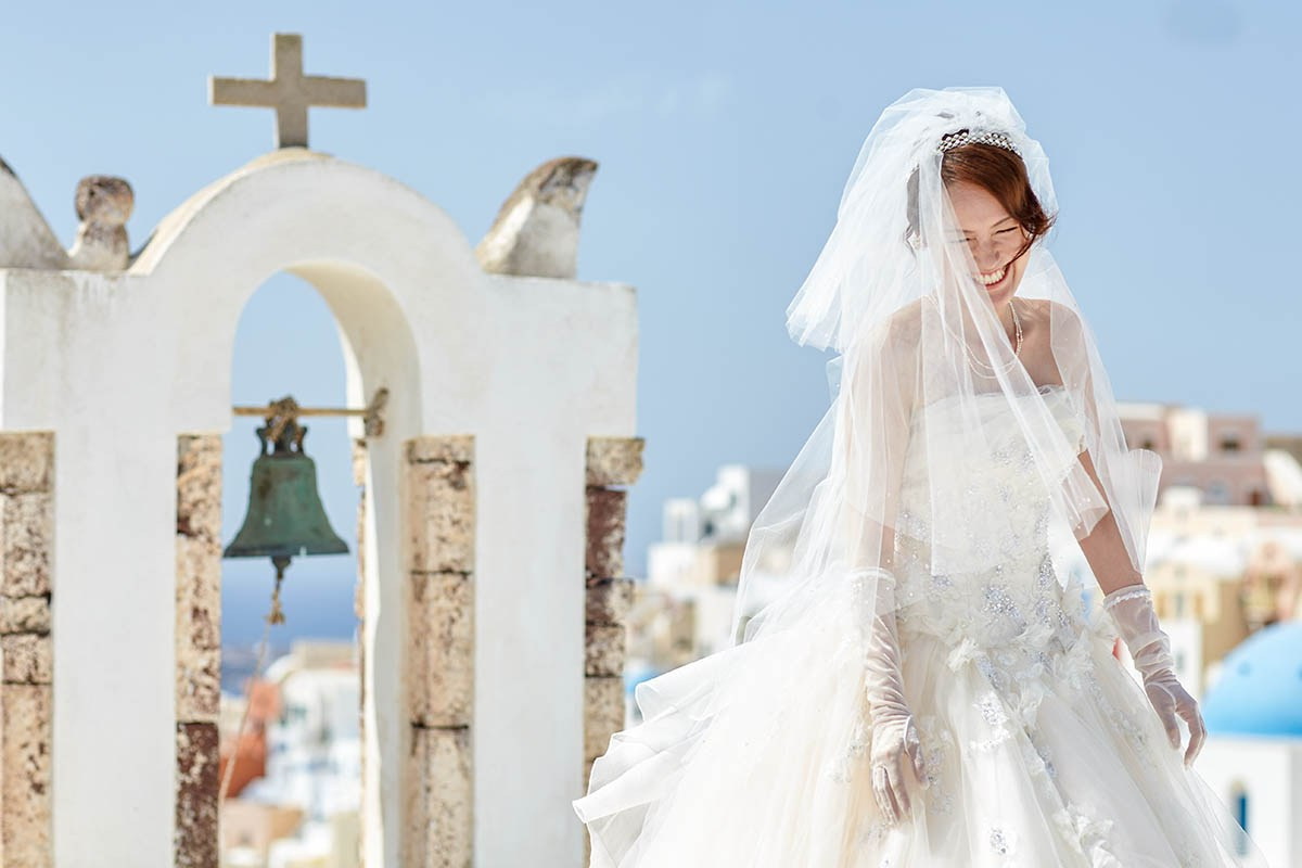 Bride laughing with joy next to a historic bell tower overlooking Santorini.