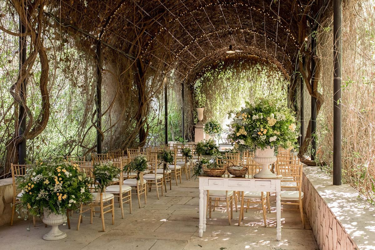 Wedding ceremony beneath a vine-covered pergola at Finca Jardines de Abril, with gold chairs, flowers and fairy lights.