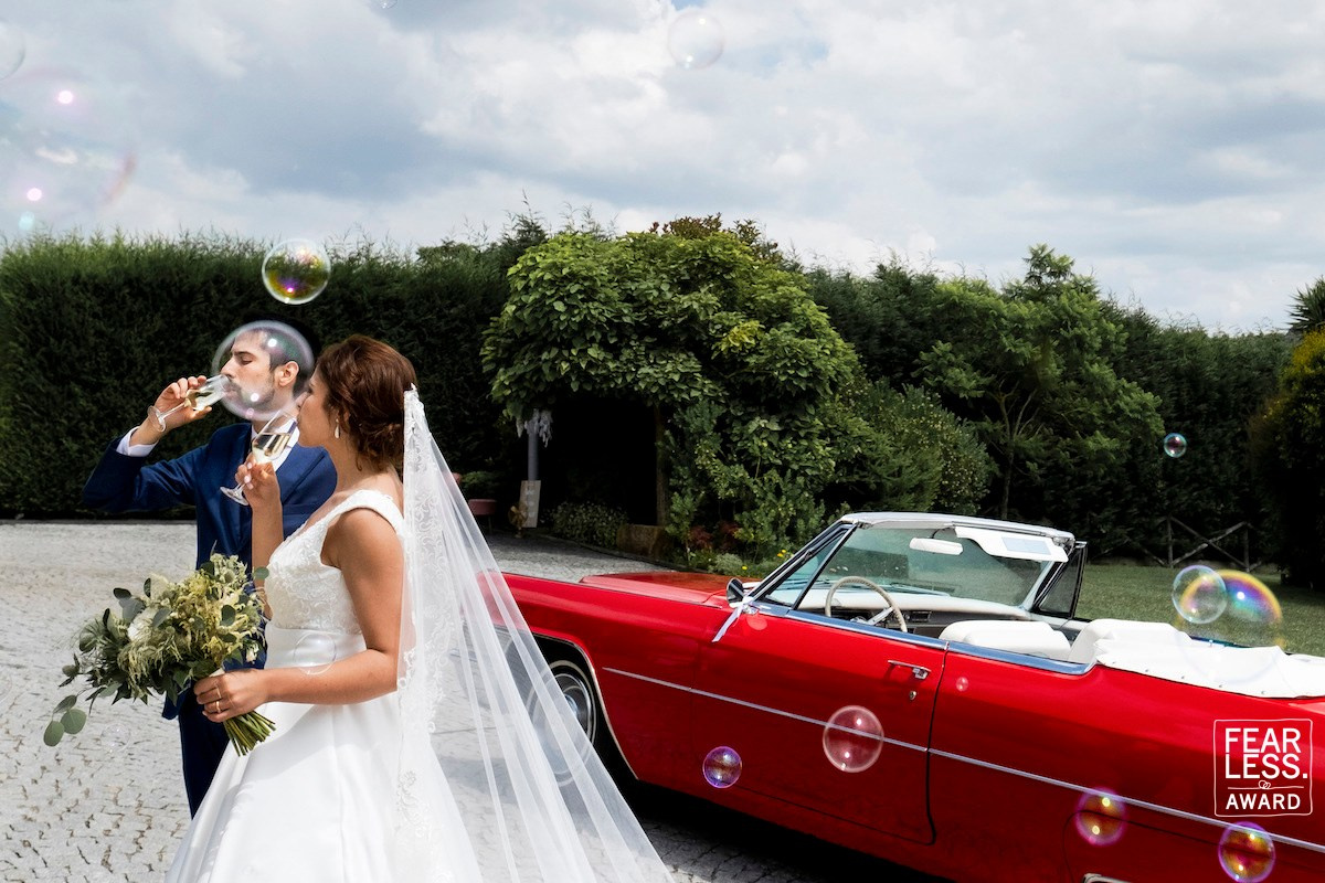 Bride and groom beside a red convertible — Fearless Award by Portugal wedding photographer Nuno Lopes