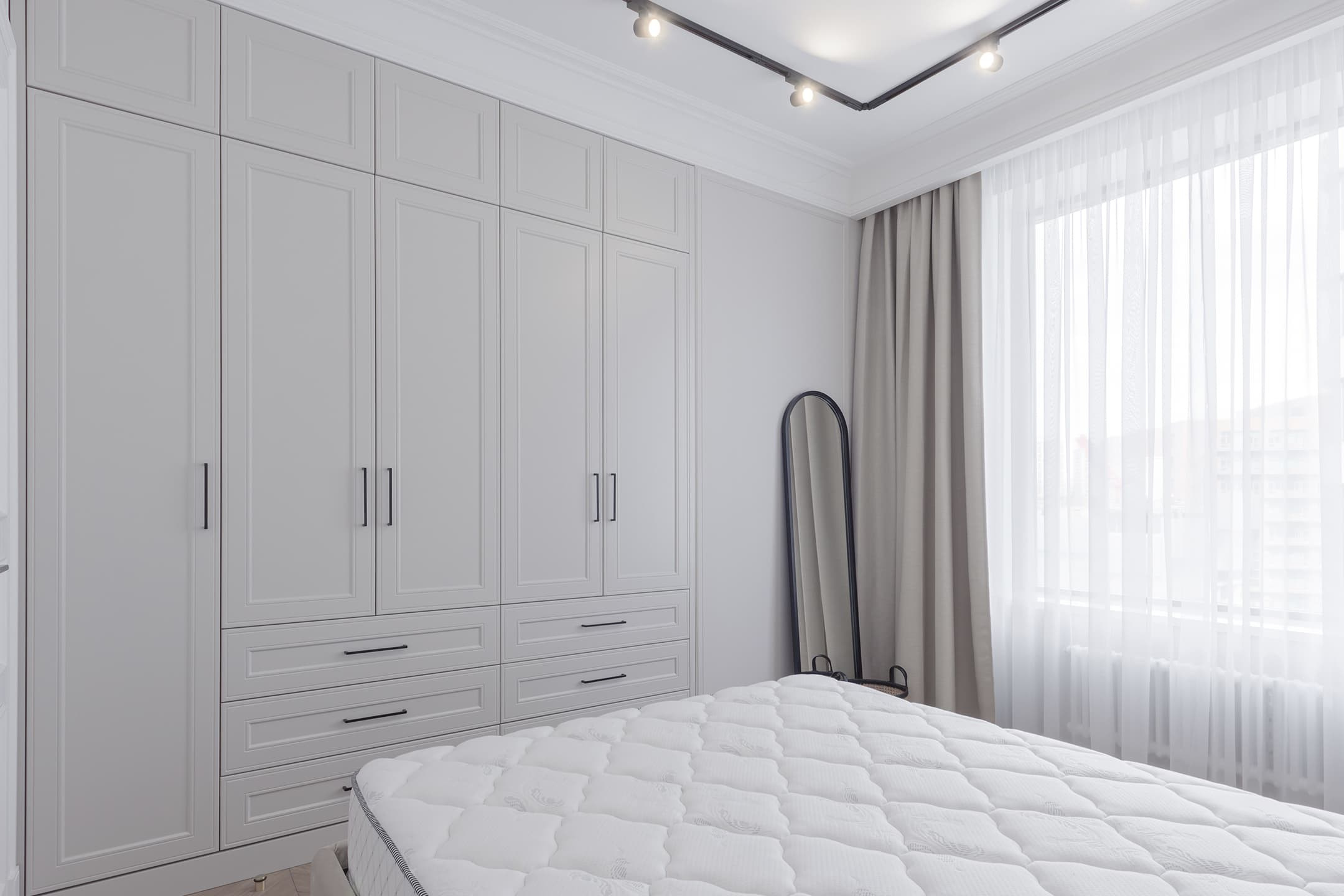 Photographie d’une chambre lumineuse avec armoire blanche et lit.