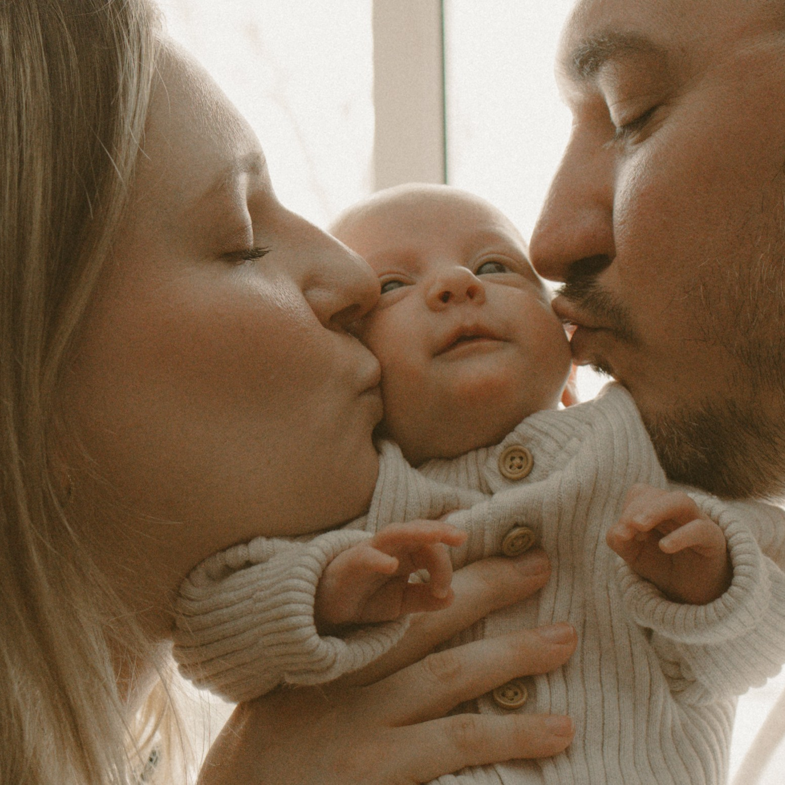 Mom and dad gently kissing their newborn baby during a heartfelt family moment