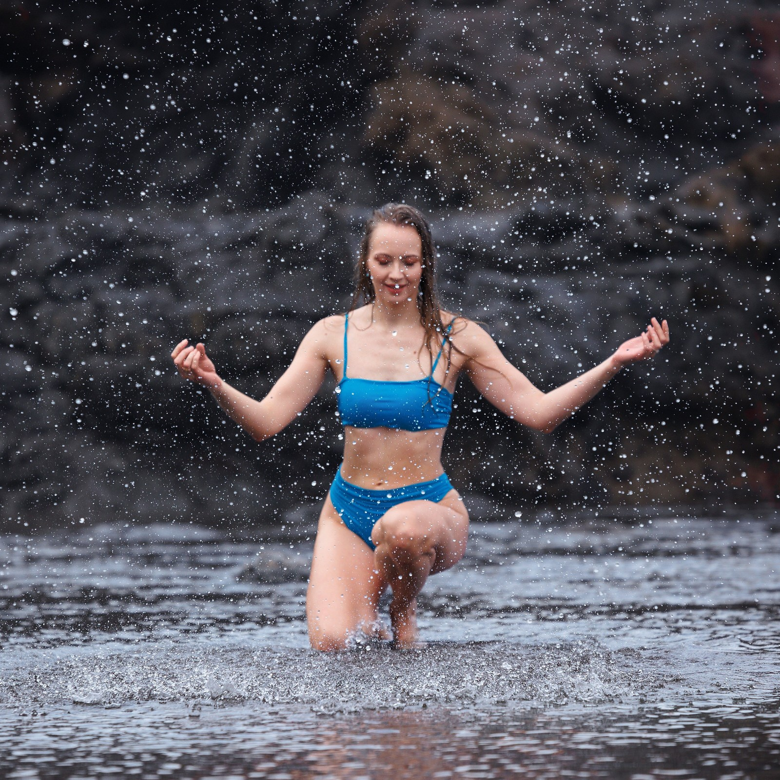 A woman in blue bikini splashing in shallow ocean water on Gran Canaria's volcanic coast