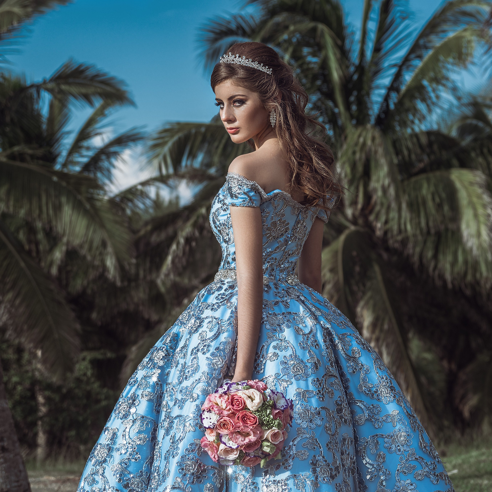 Quinceañera con vestido azul bordado frente a palmeras, fotografía de XV años en México, fotógrafo Carlos RaGo Coatzacoalcos