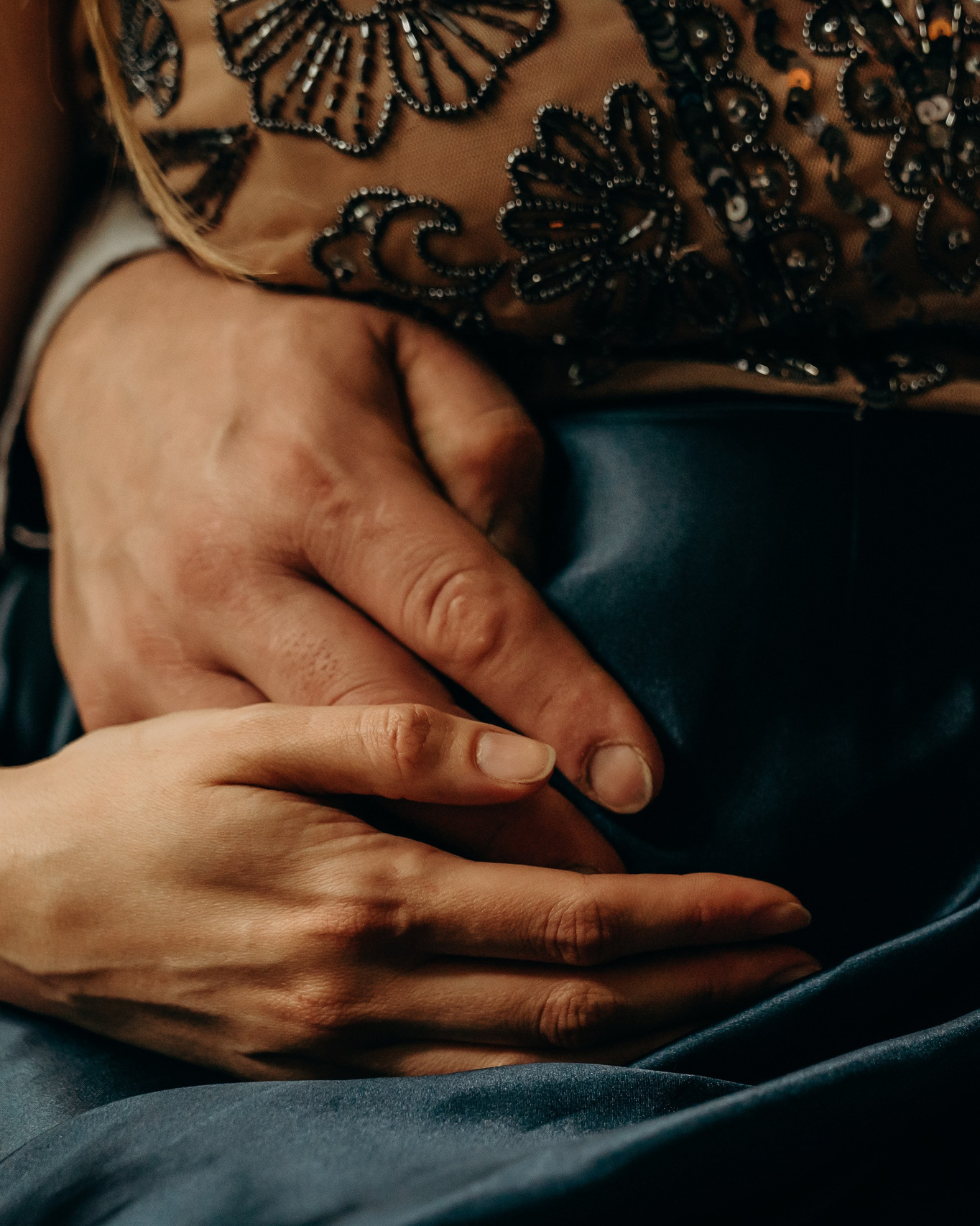 Close-up of expectant parents' hands resting on a pregnant belly, photographed in soft natural light.