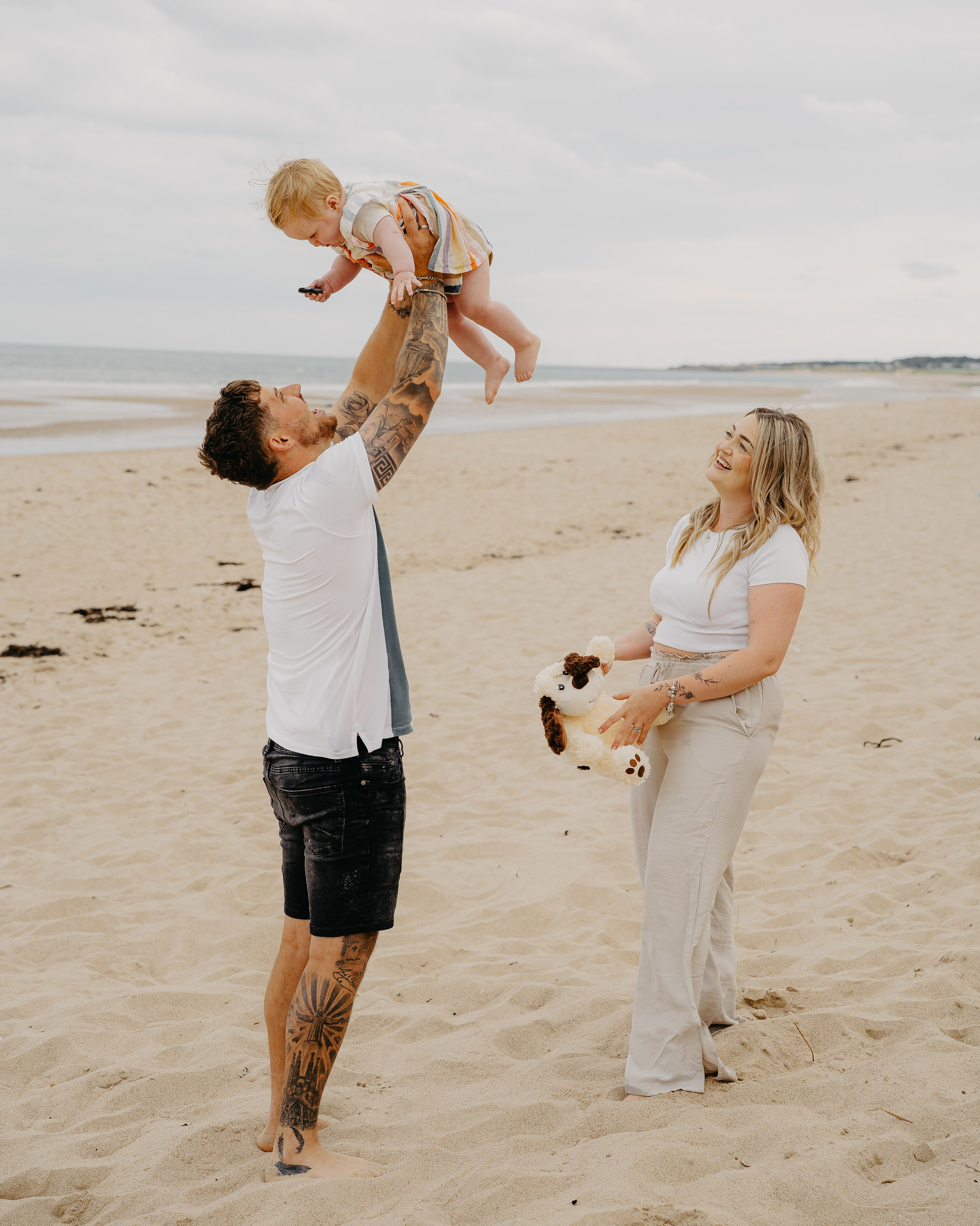 Parents playing with their young child on the beach during a natural family photoshoot at Creswell Beach, Northumberland.