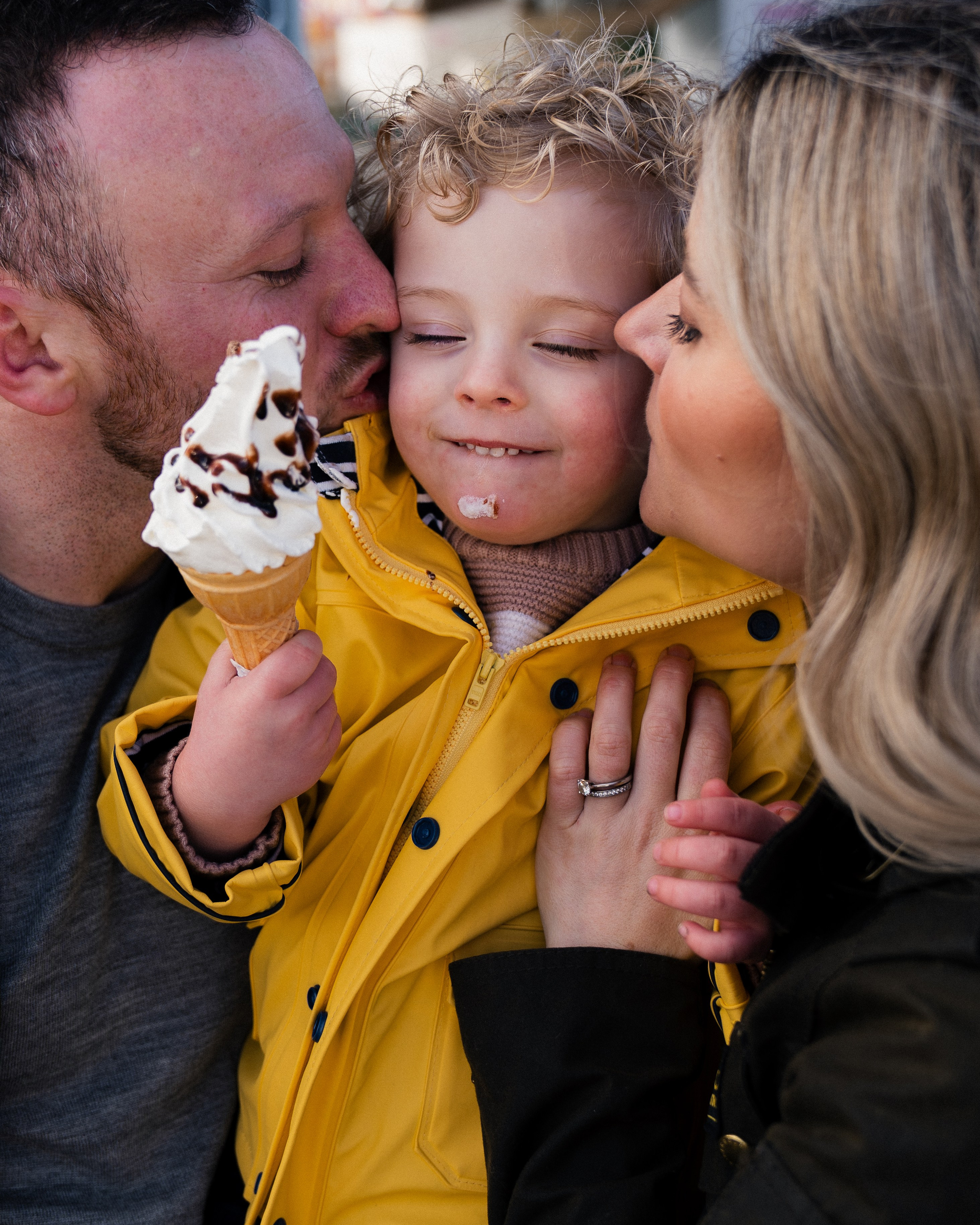 Parents kissing their child during a natural family photoshoot in Whitley Bay, capturing a warm and candid spring moment