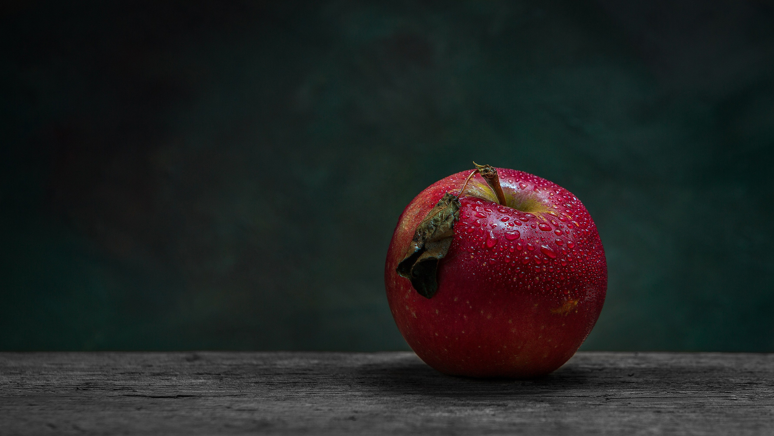 Tünd fonda və taxta səth üzərində su damcıları ilə örtülmüş klassik qırmızı alma fotoşəkli – natürmort qida vizualı