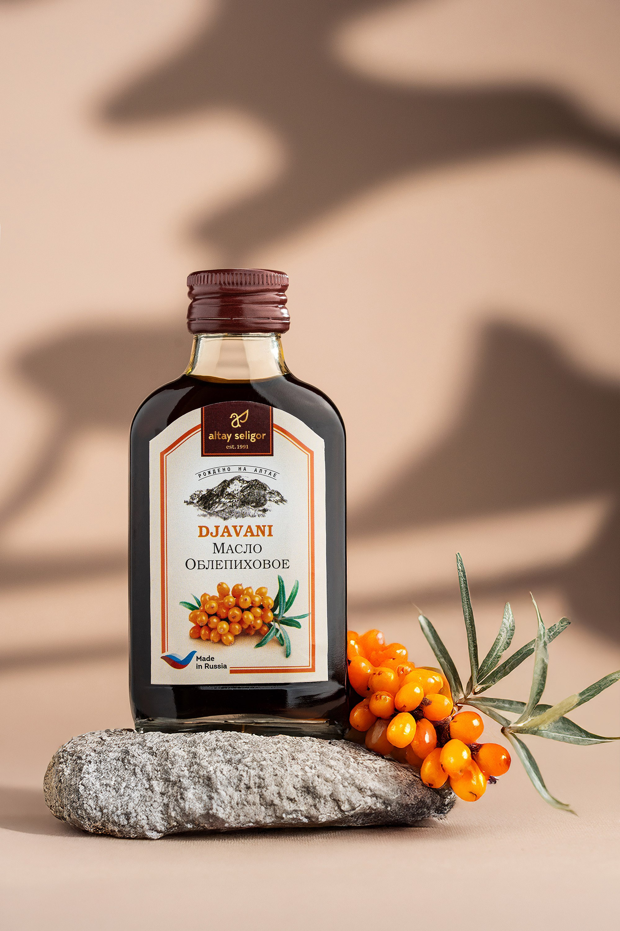 Təbii daş üzərində dayanan DJAVANI dəniztikanı yağı butulkası, yanında meyvə və yarpaq ilə birlikdə, arxa fonda yumşaq kölgə effektləri.