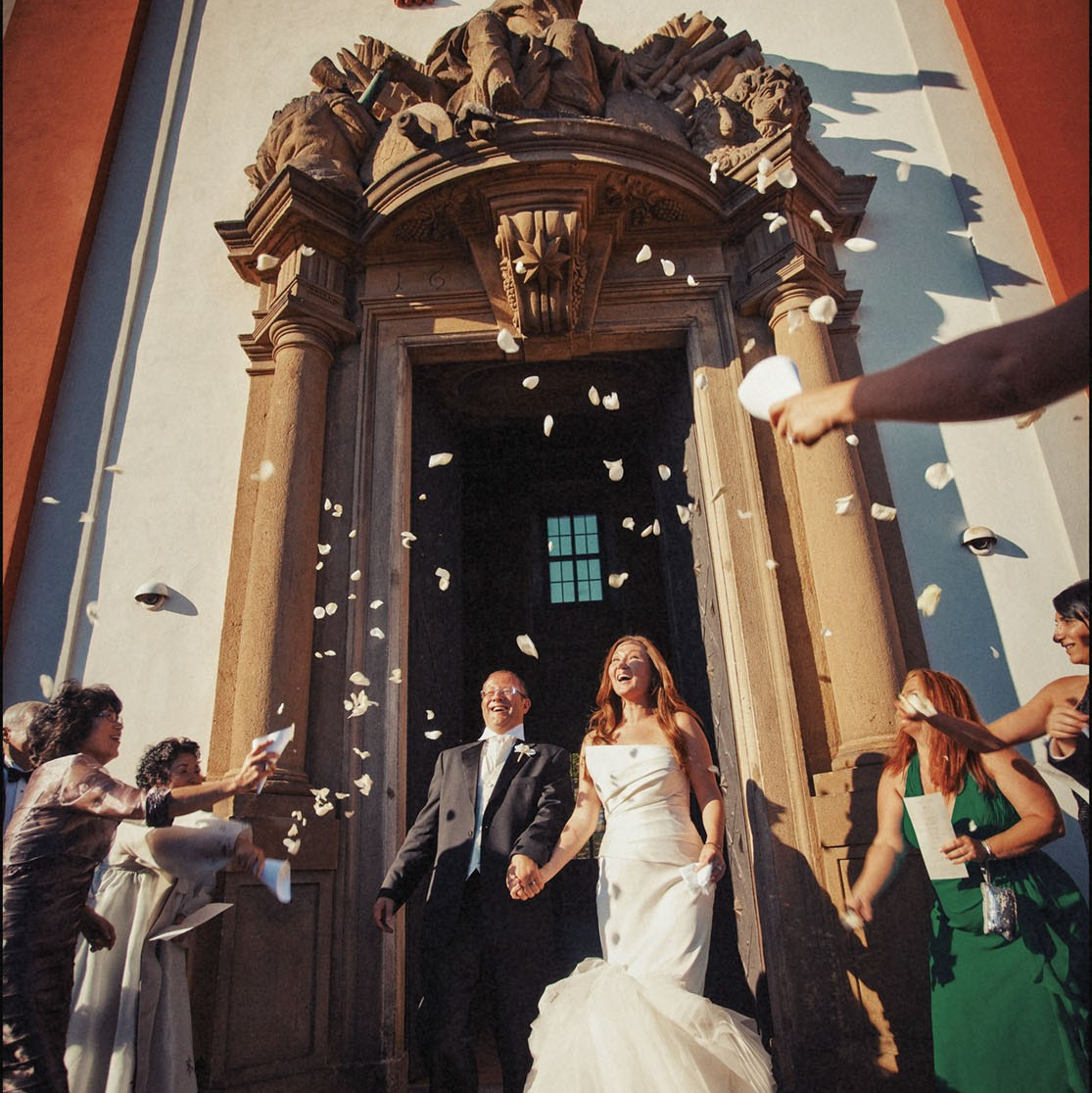 Elegant couple are welcomed with rice and rose petals as they exit the historic facade of the Troja Chateau on their wedding day.