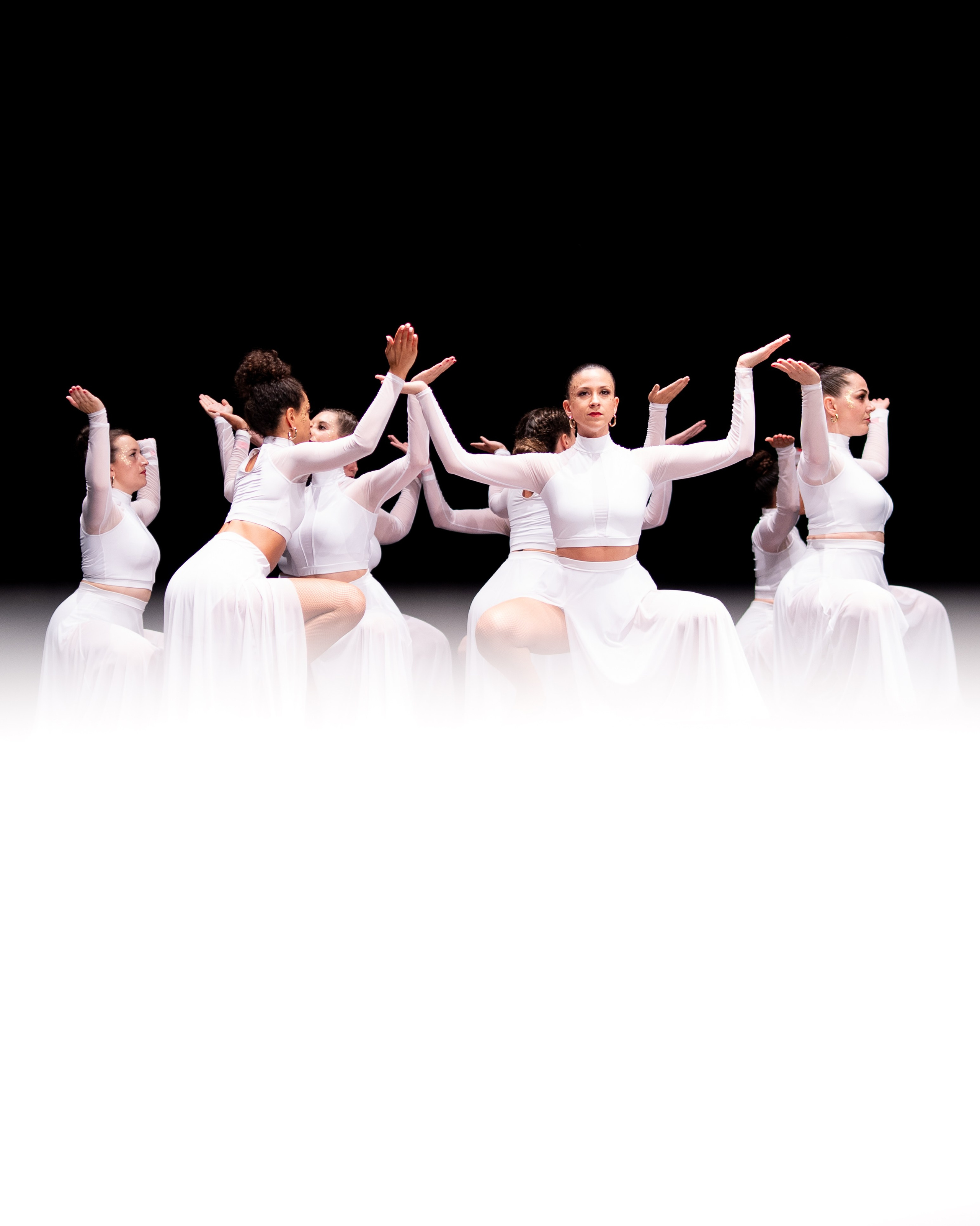 Groupe de danseuses en costumes blancs sur scène noire.