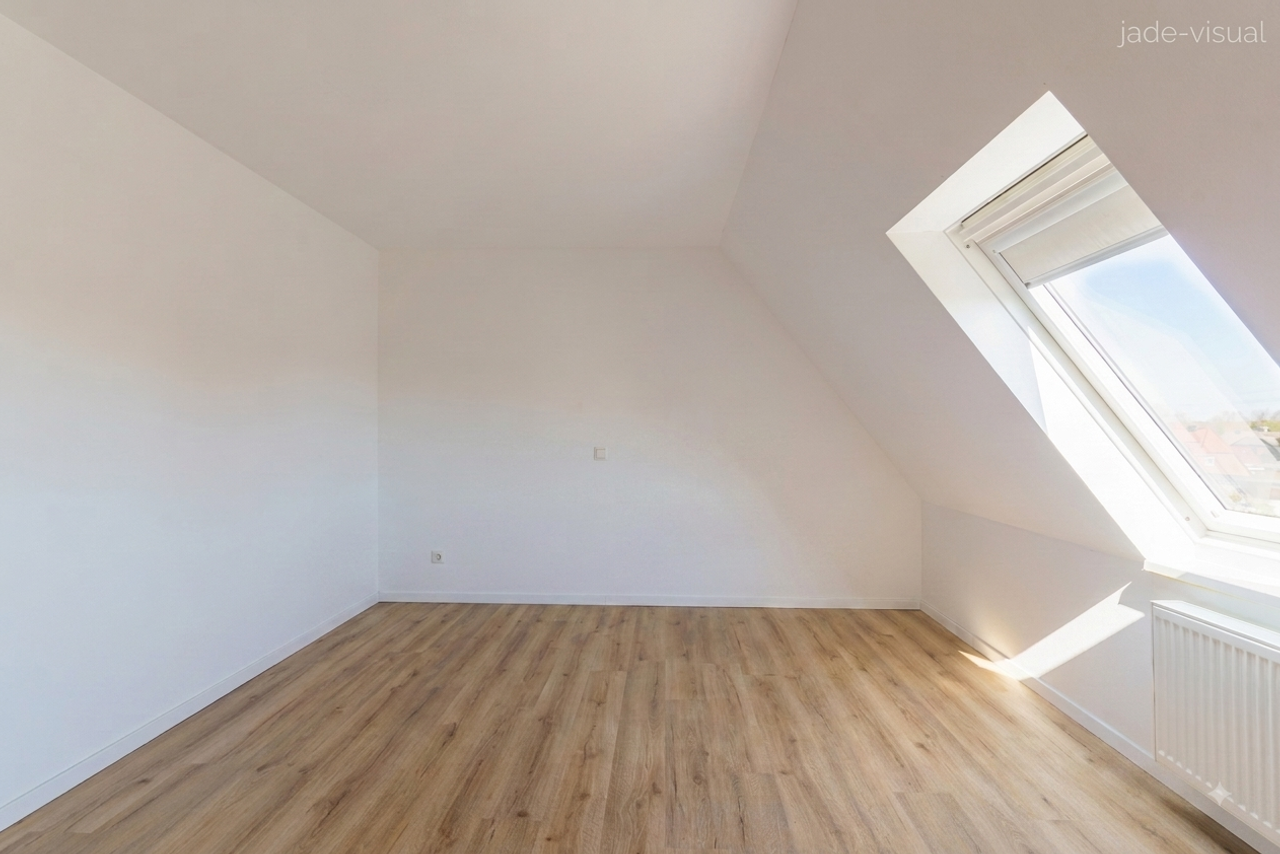 KI-leergeräumtes Schlafzimmer im Dachgeschoss (virtuelles Decluttering) mit Dachfenster, Heizkörper und Laminatboden. Fotoservice von jade-visual.