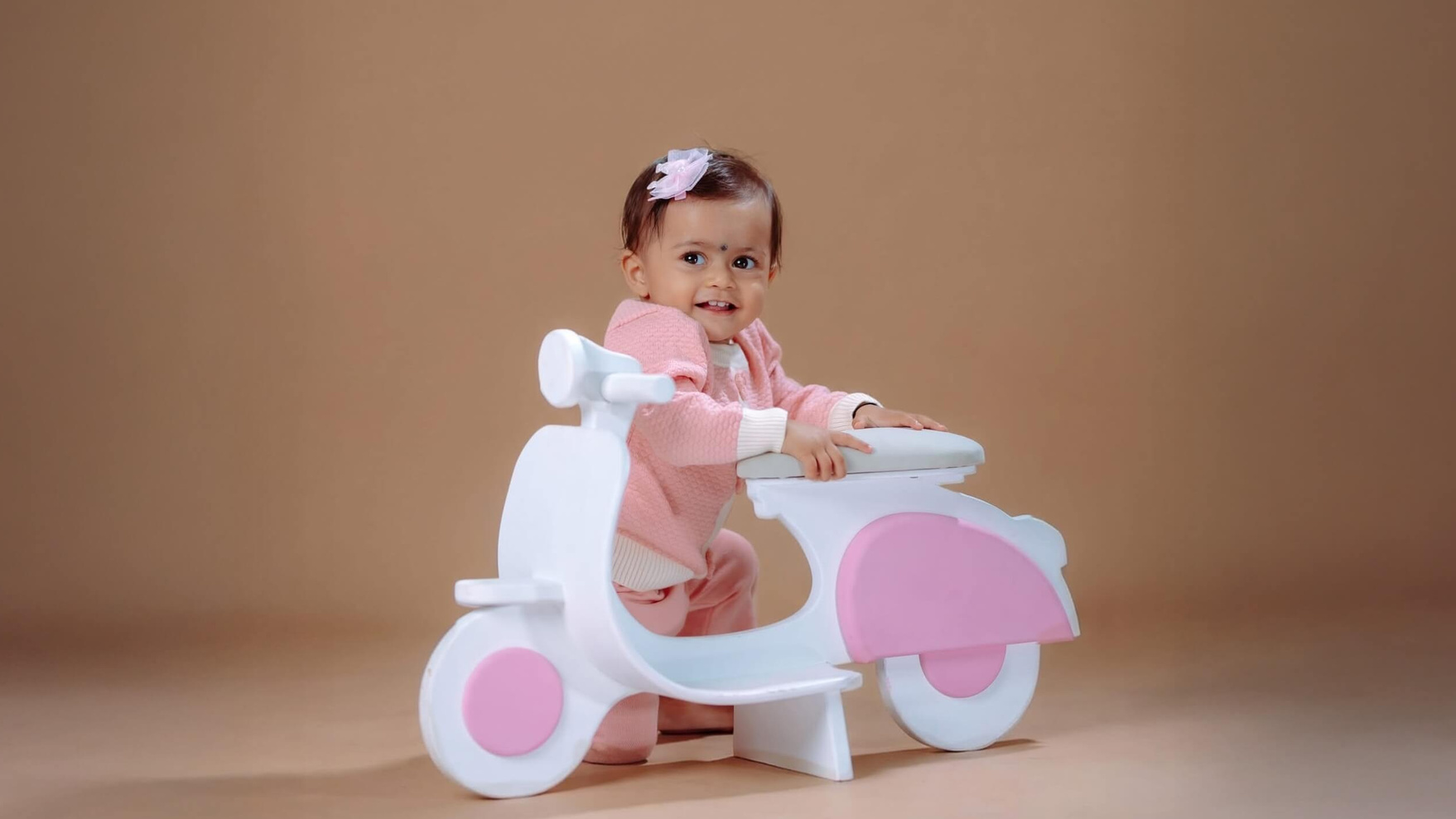 Baby girl on a pink toy scooter during a studio photography session in Butwal