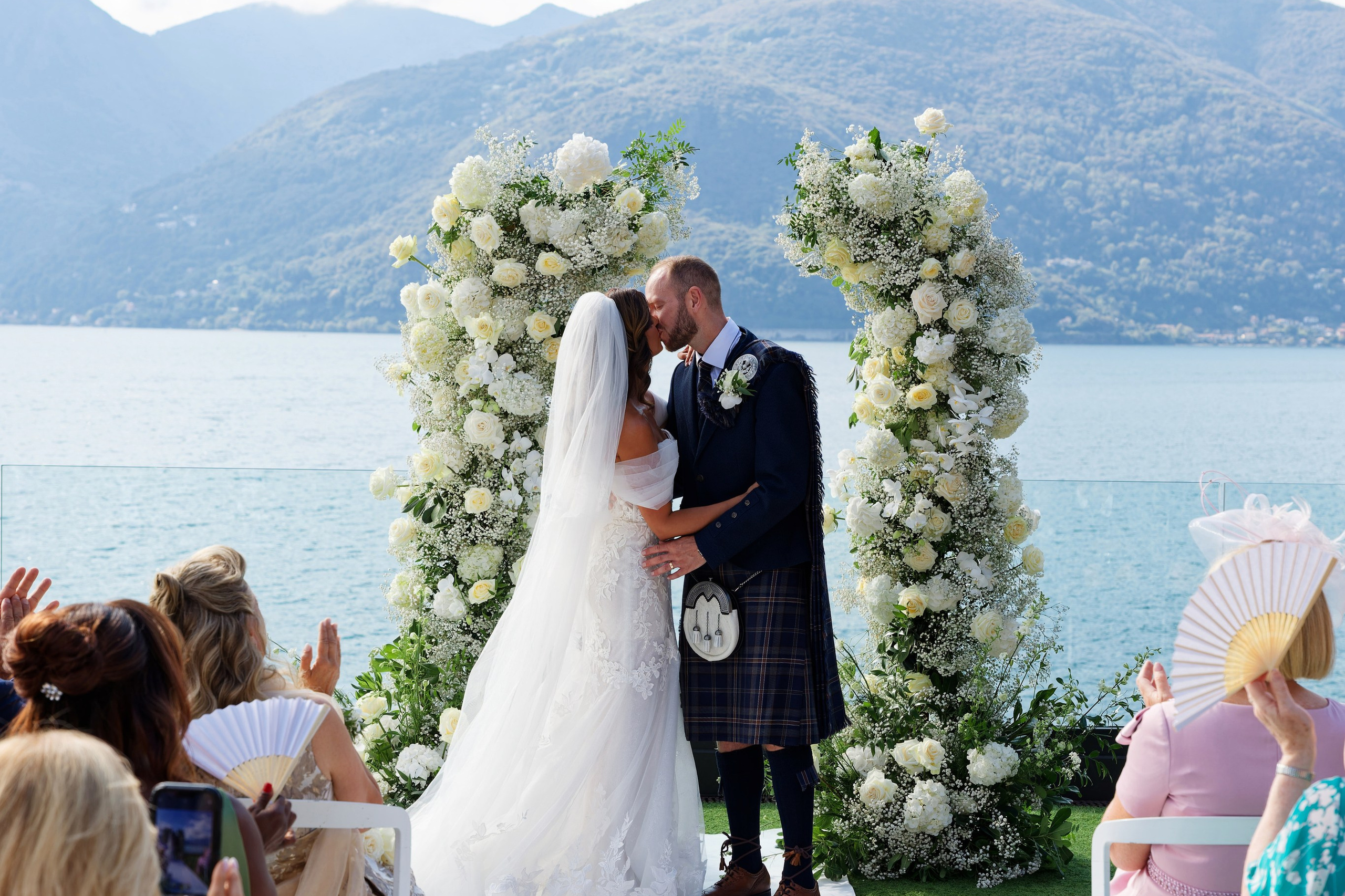 Eine Braut und ein Bräutigam umarmen sich vor einem See.