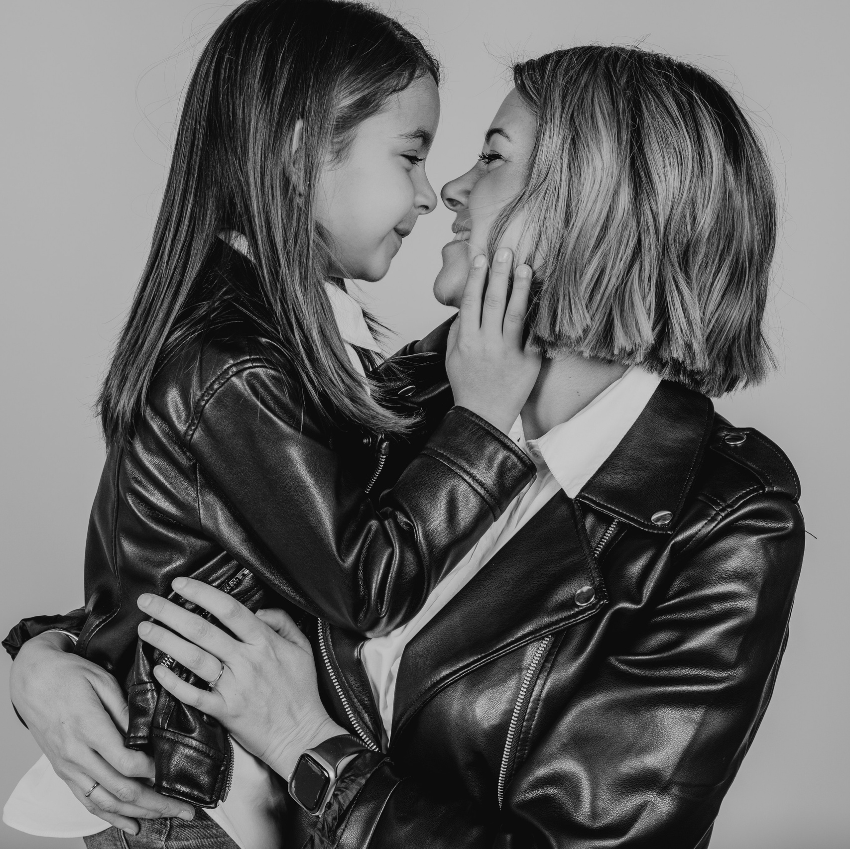 Mamá y su hija pequeña posando juntas en una sesión de fotos en estudio, ambas luciendo chaquetas de piel, capturando un momento de ternura y estilo familiar
