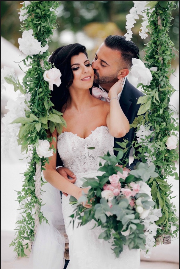 Жених и невеста на качелях в ресторане, жених целует невесту в шею, а невеста нежно обнимает жениха. 