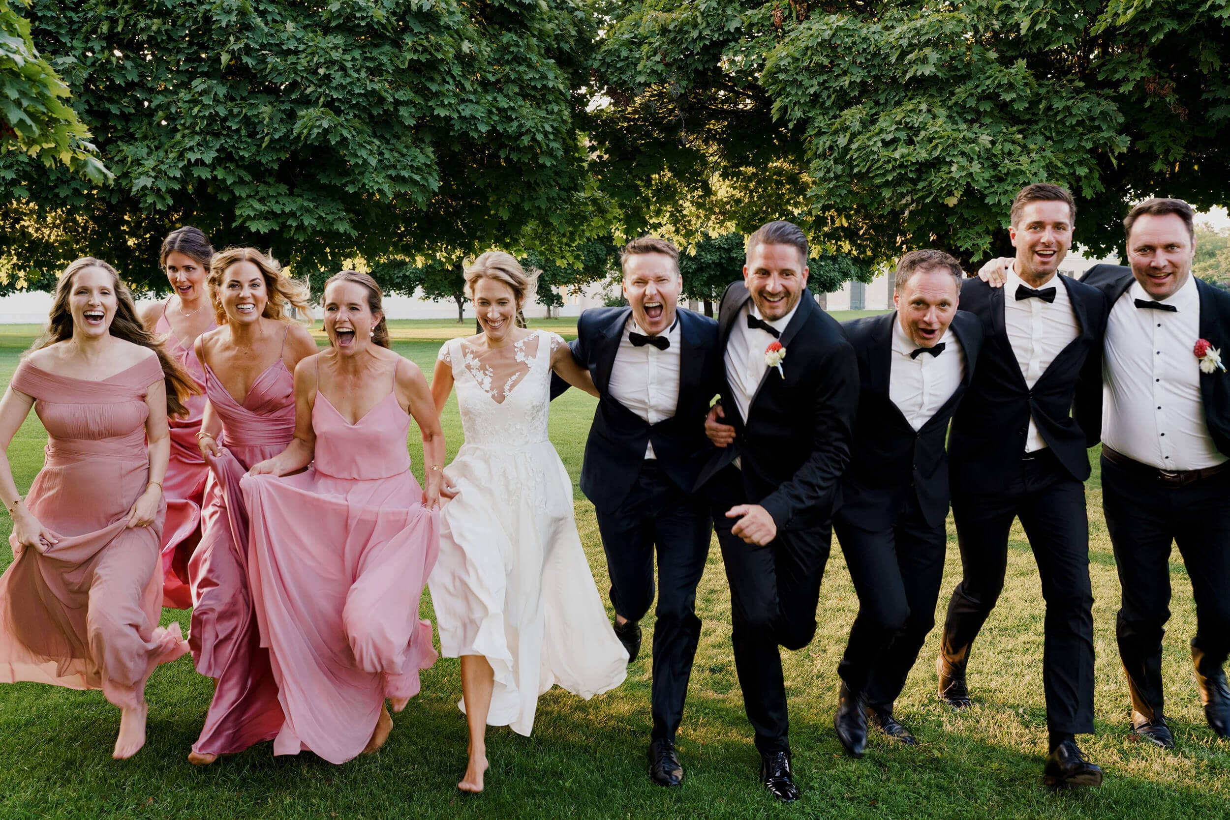 Gruppenbild von Brautleuten, die auf den Fotografen zulaufen, sich umarmen und lächeln