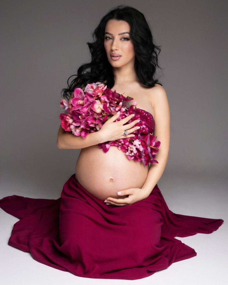 Donna incinta in abito bordeaux durante un servizio fotografico maternity elegante in studio a Padova.