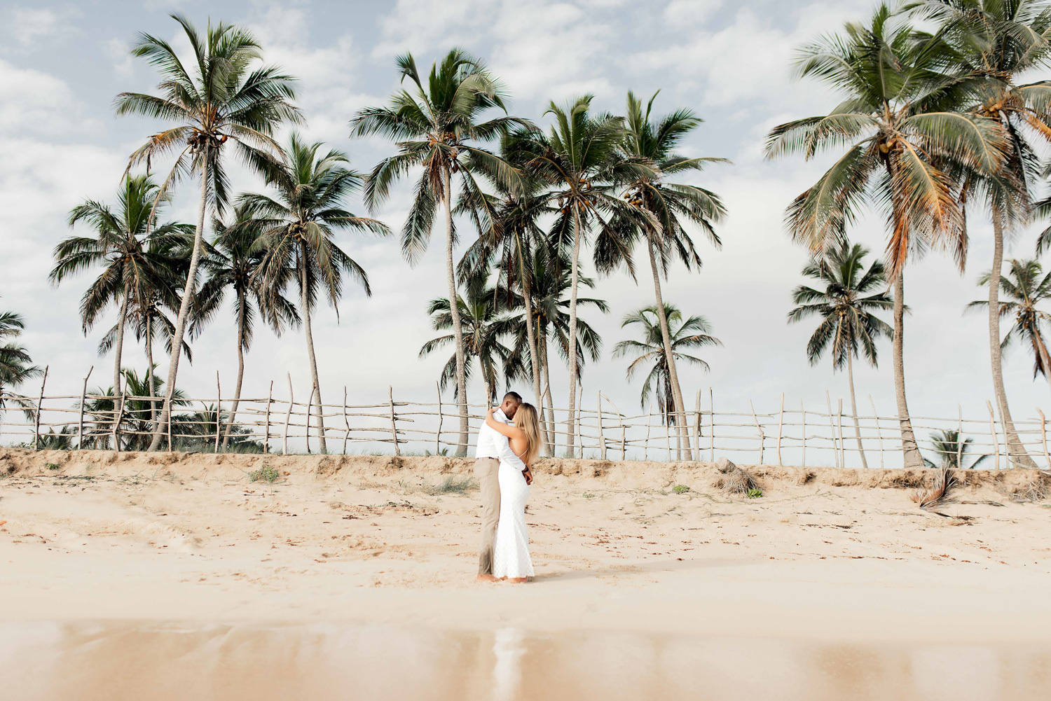 Newlyweds kissing in front of palm trees on Macau beach. 
