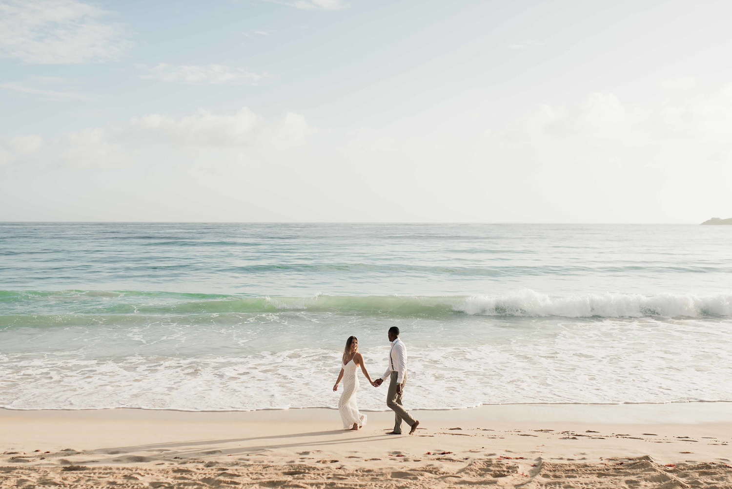 The bride and groom walk on the beach during a photo shoot at sunrise. 