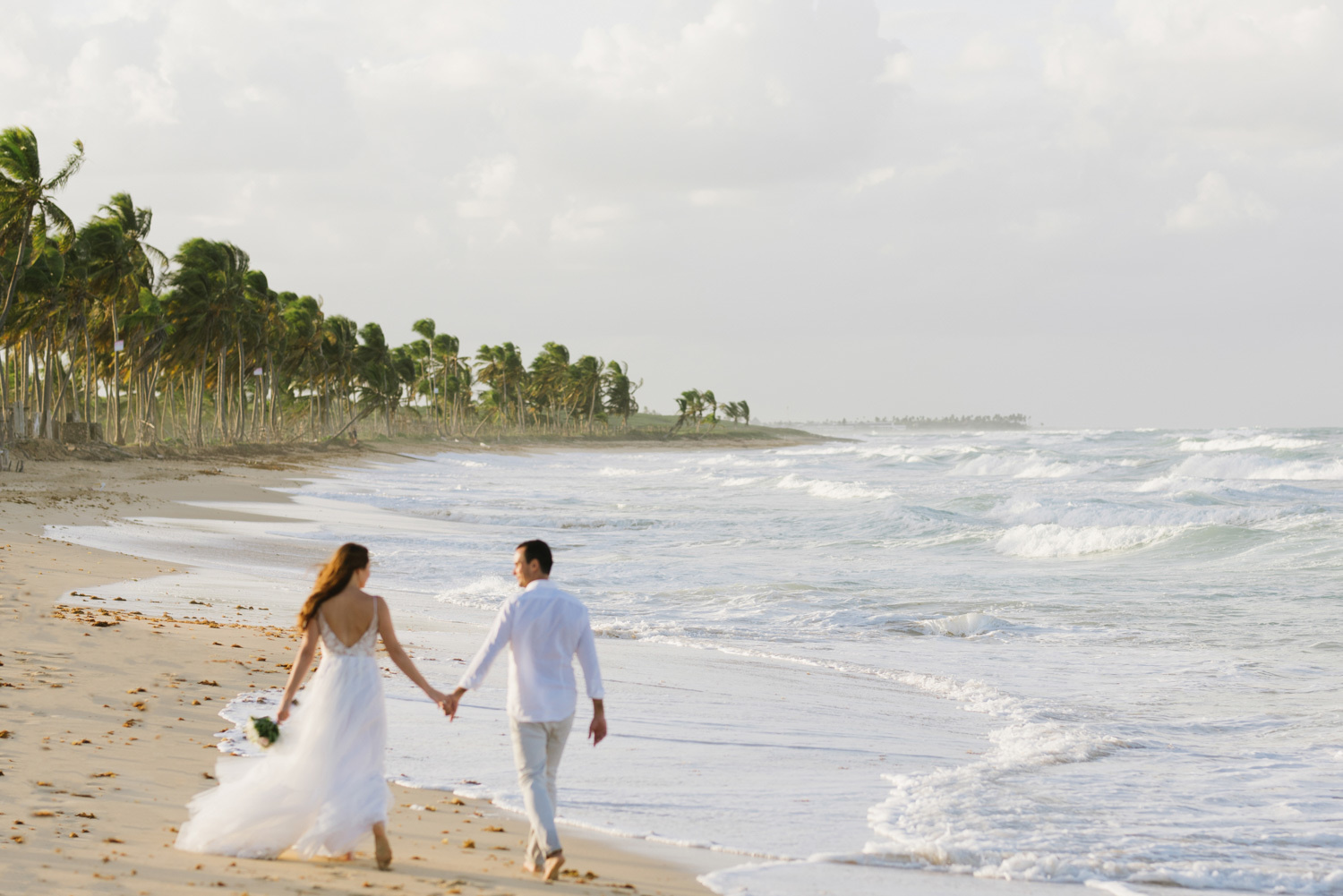 The bride and groom walk hand in hand, walking away from the photographer into the ocean's sharecropper.