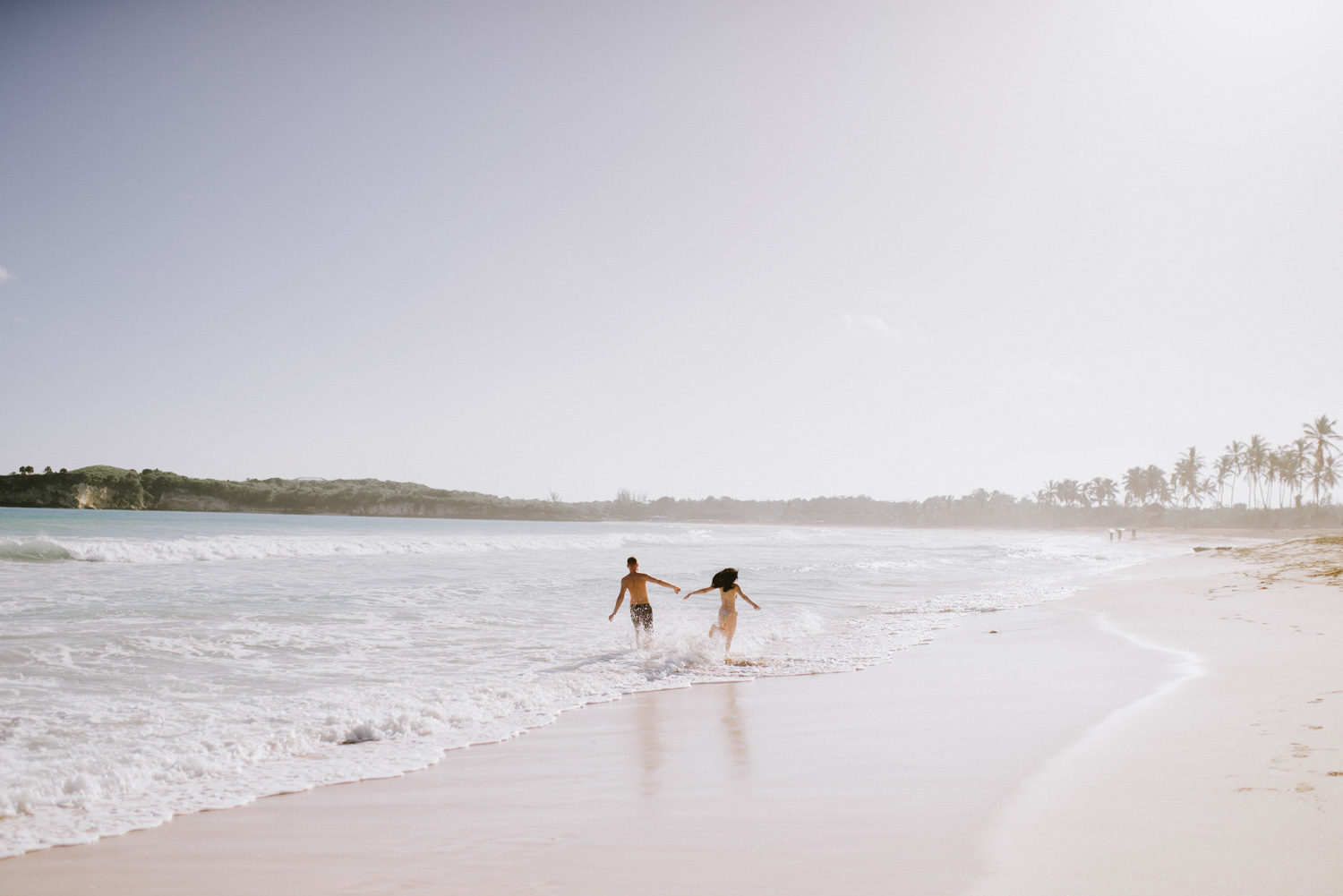 Молодожены бегут по волнам взявшись за руки. 