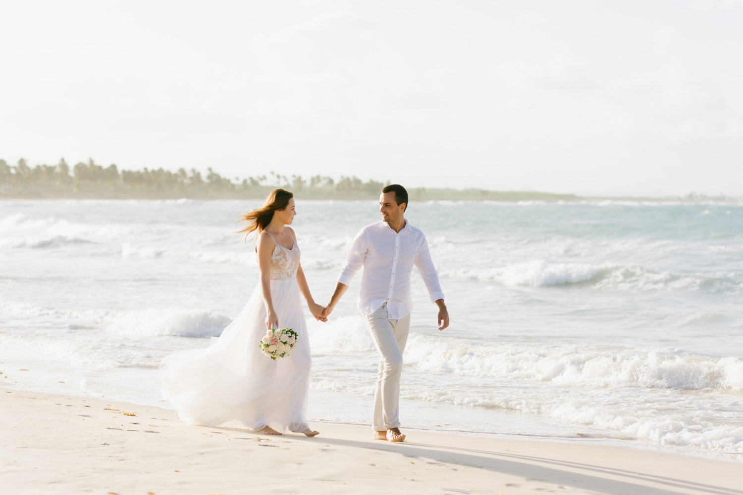 The newlyweds walk hand in hand to the shoreline sharecropper holding hands.