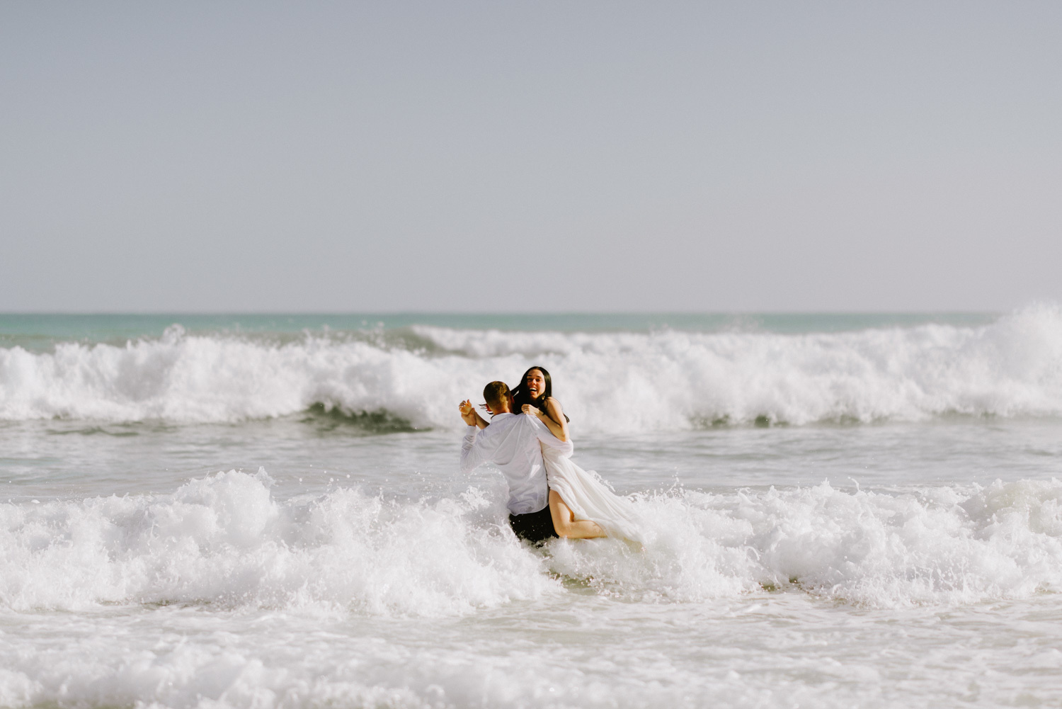 Жених бросает невесту в океан, это весело и все улыбаются. 