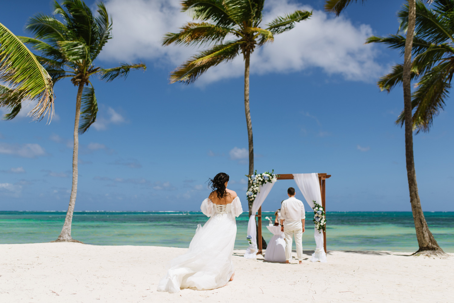 Невеста в роскошном свадебном платье идет к арке где ее ждет жених.