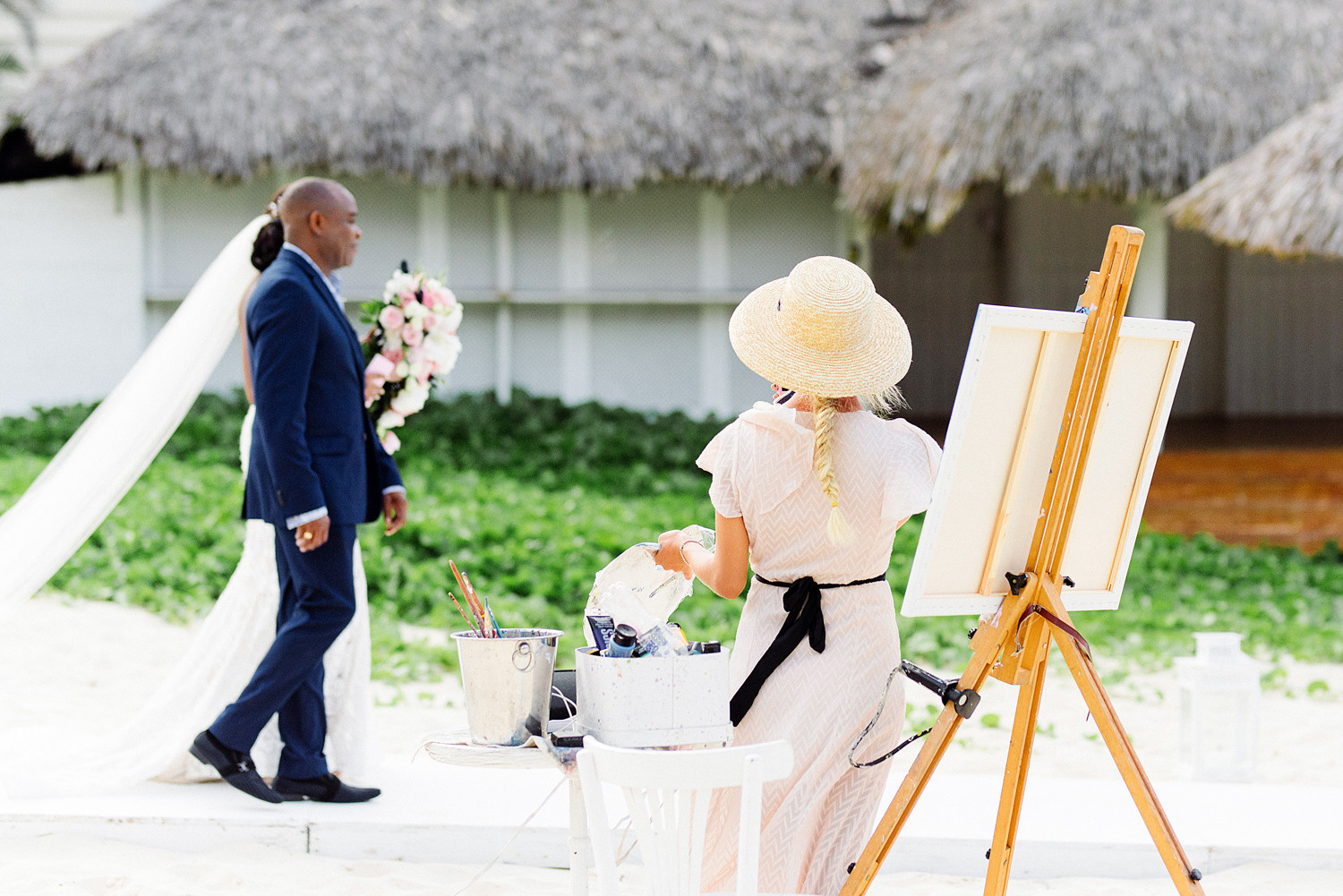 Художник рисует свадьбу, в этот момент проходит невеста с женихом, у невесты длинная фата а у жениха классический пиджак.