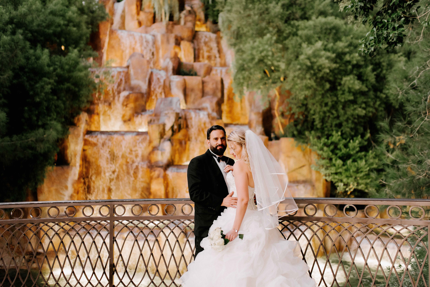 Жених смотрит в камеру на фоне фонтана в отеле Цезарь палас а невеста обнимает его за талию. 