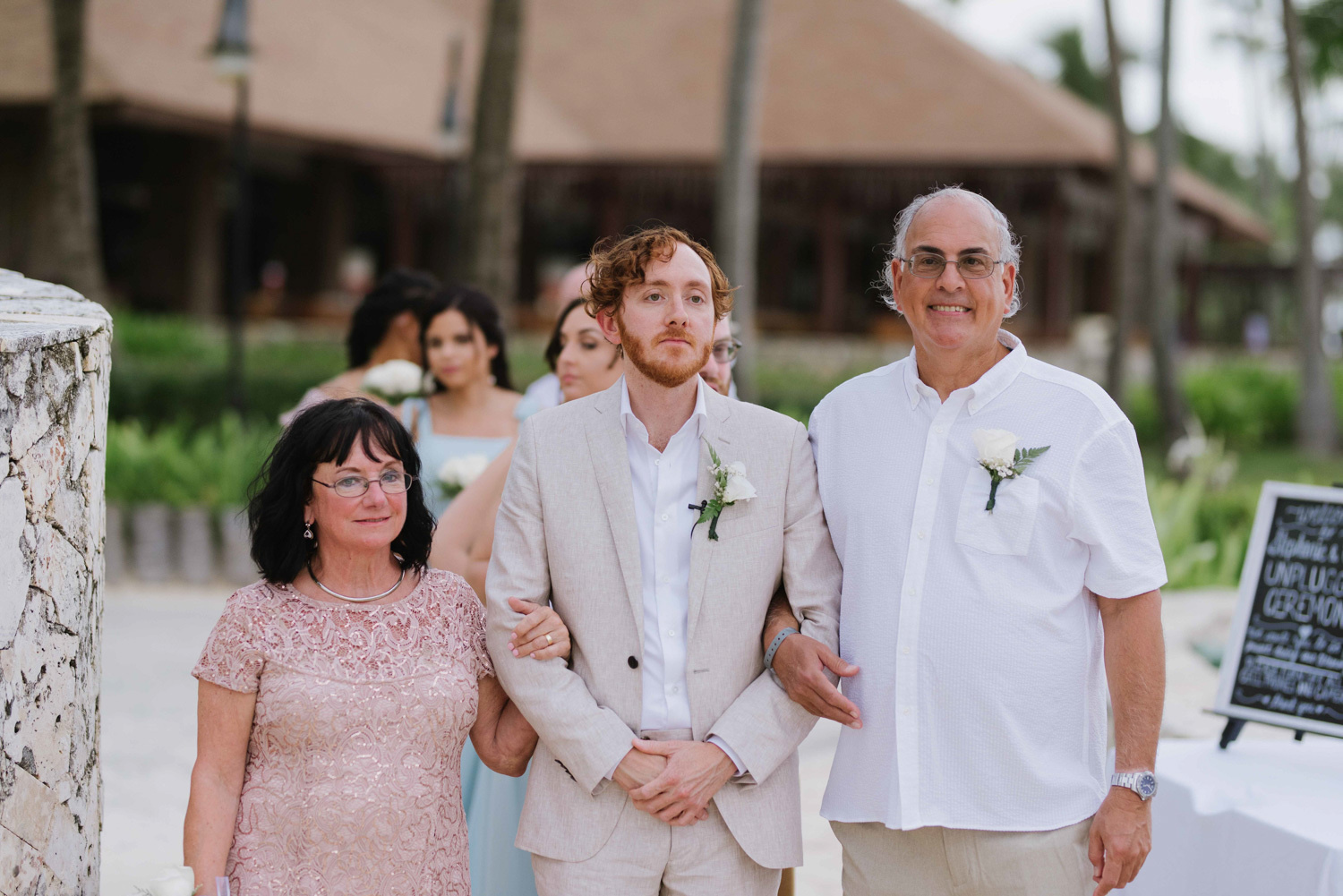 The mother and father lead the groom down the aisle. 