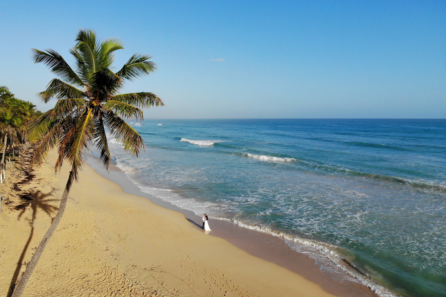Фотография сделанная с квадрокоптера, жених и невеста стоят возле океана взявшись за руки. 