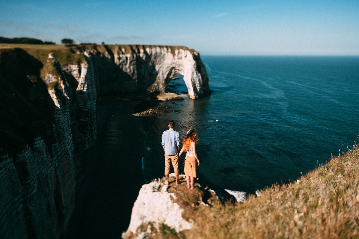 The groom holds the bride's hand against a backdrop of white cliffs on a beach in Normandy. 