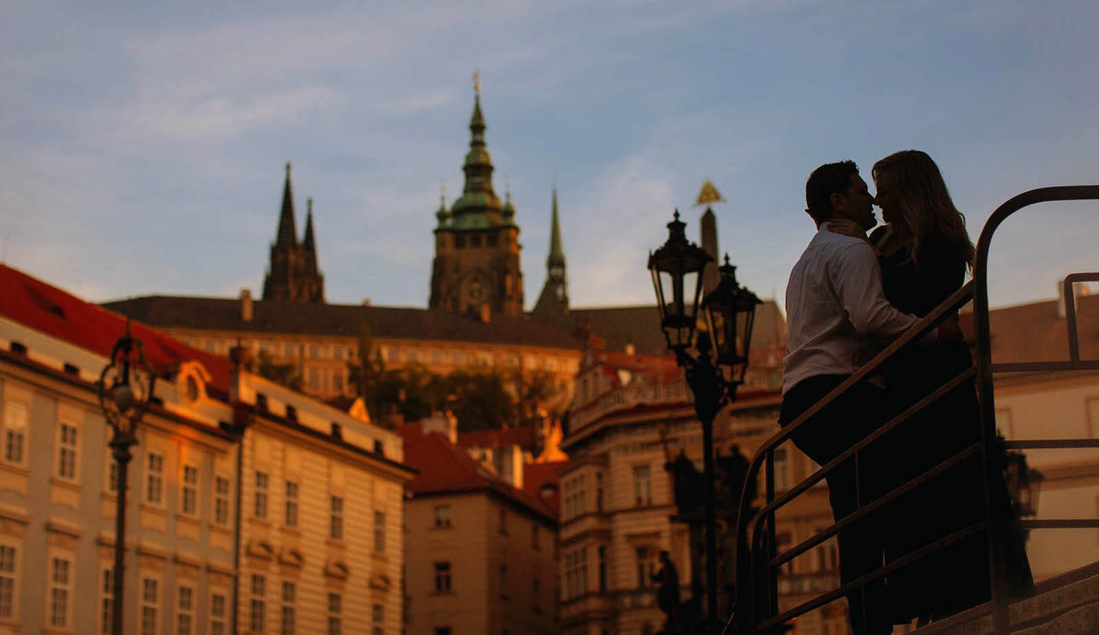 An American couple silhouetted against soft morning light above the rooftops of Prague from Prague Castle