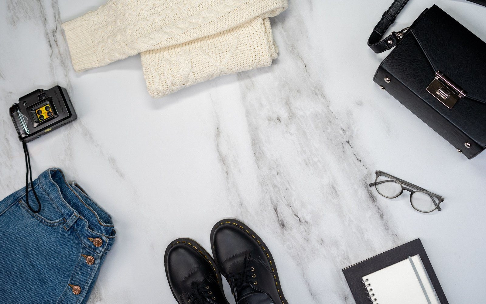 Flat lay of folded clothing, jeans, black shoes, a handbag and accessories