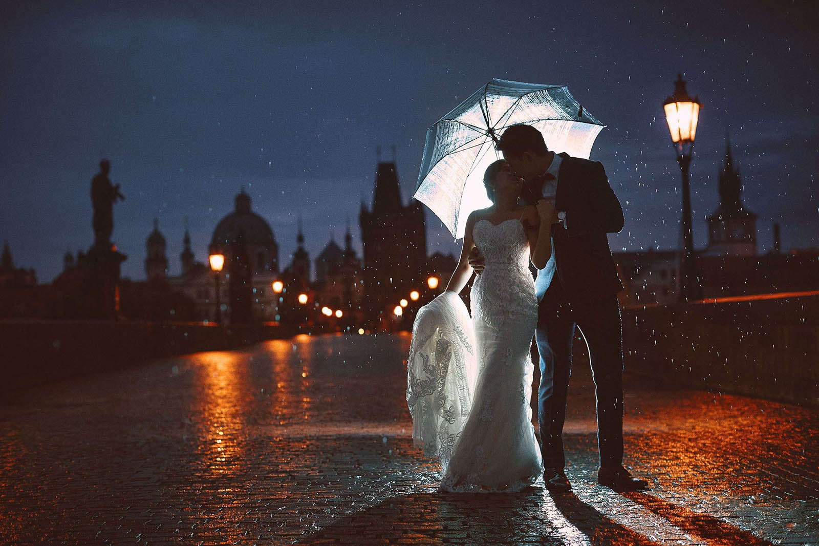 Cinematic pre-wedding photography — couple walks above the Strahov vineyards as sunrise illuminates Prague Castle and the city skyline below — Kurt Vinion Photography
