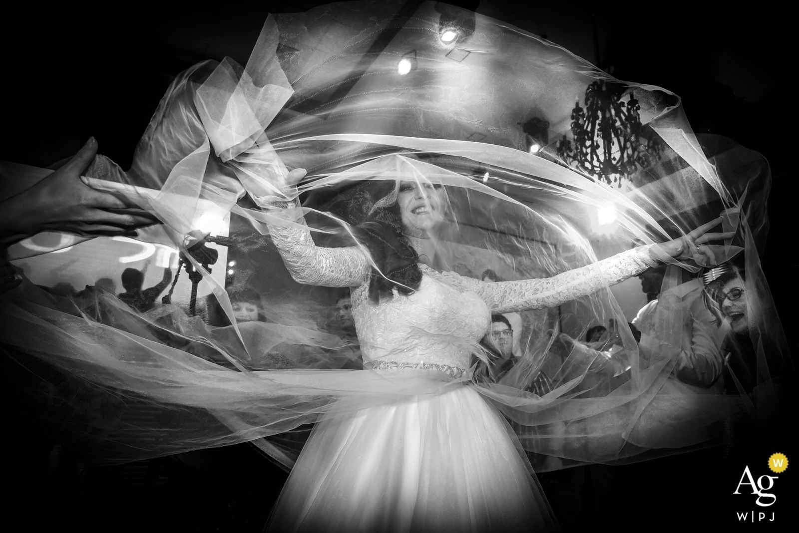 An emotional black-and-white shot: the bride at the center, wrapped in the movement of her veil. Her joy and the guests' reactions create a powerful celebratory atmosphere.