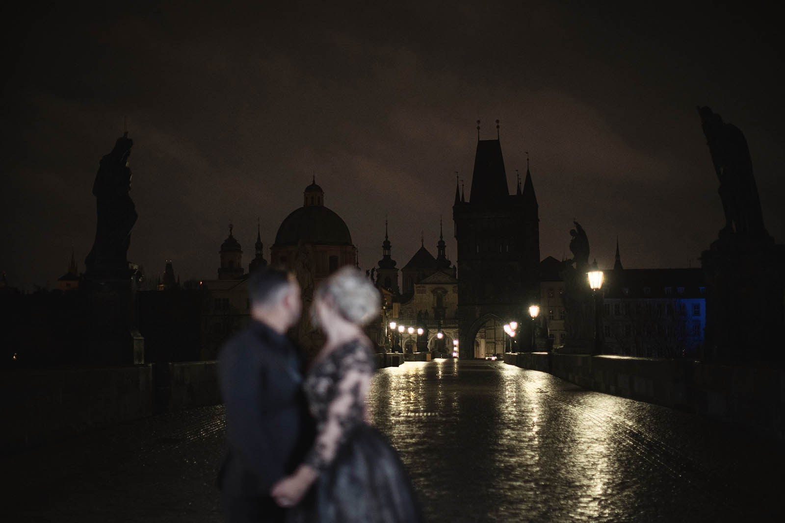 Couple in black silhouetted against the nighttime landscape of a rainy Charles Bridge