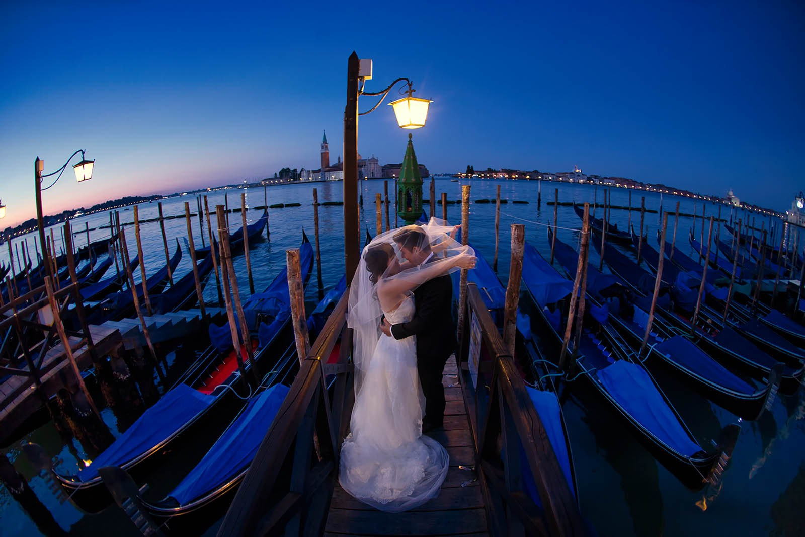 Art-directed pre-wedding portrait — bride covers her groom's face with her veil as they stand above a gondola canal in Venice at dawn — Kurt Vinion Photography