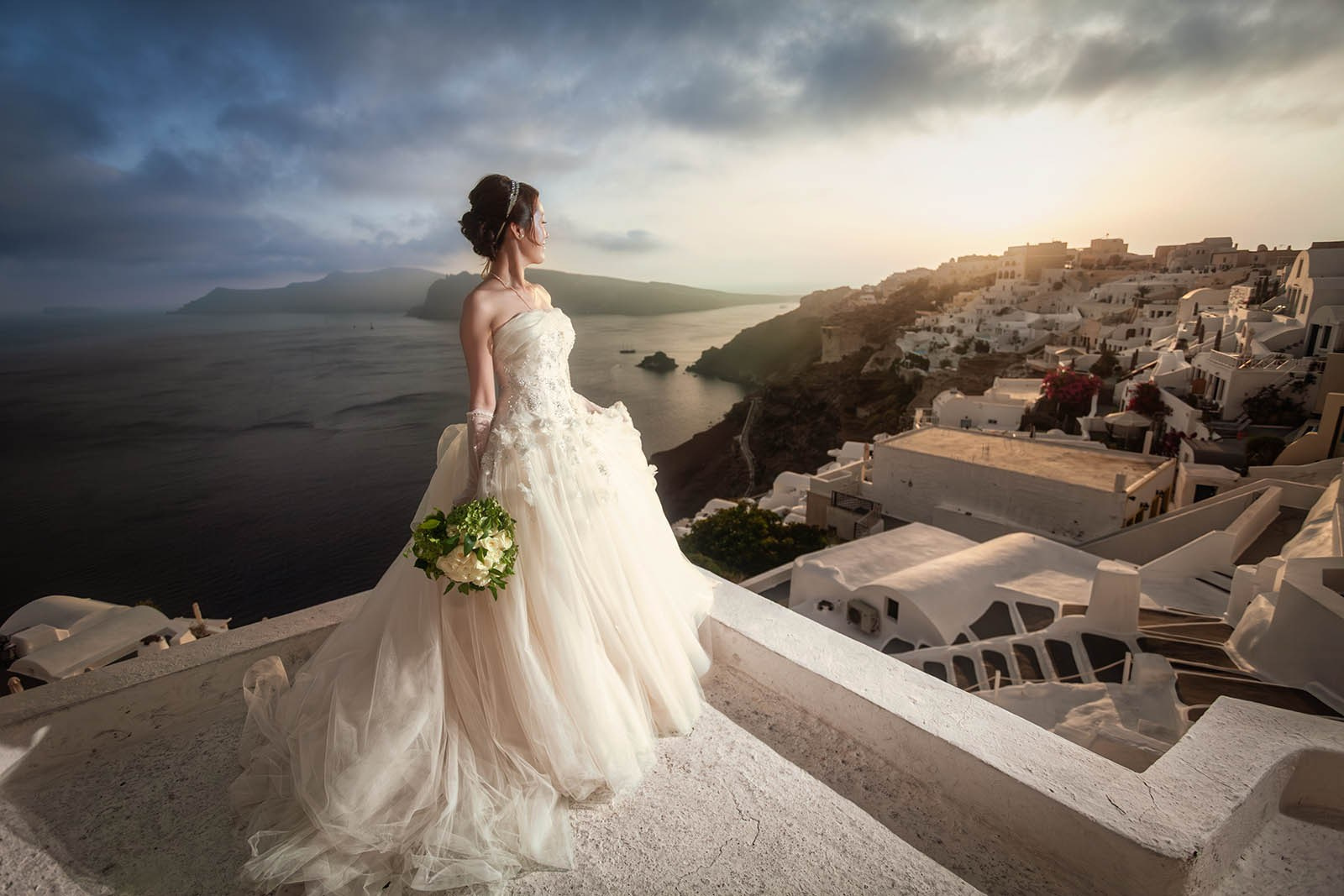 Bride at sunset looking toward the light over the caldera in Oia, Santorini.