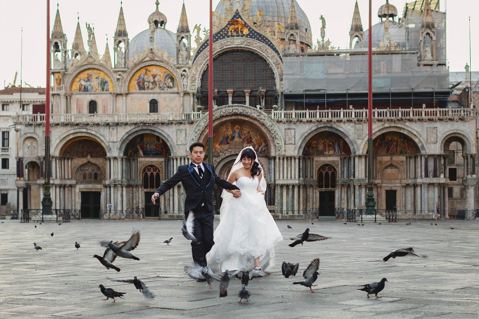 Asian newlyweds run through the pigeons in an empty St. Mark's Square in Venice, Italy - Kurt Vinion Photography
