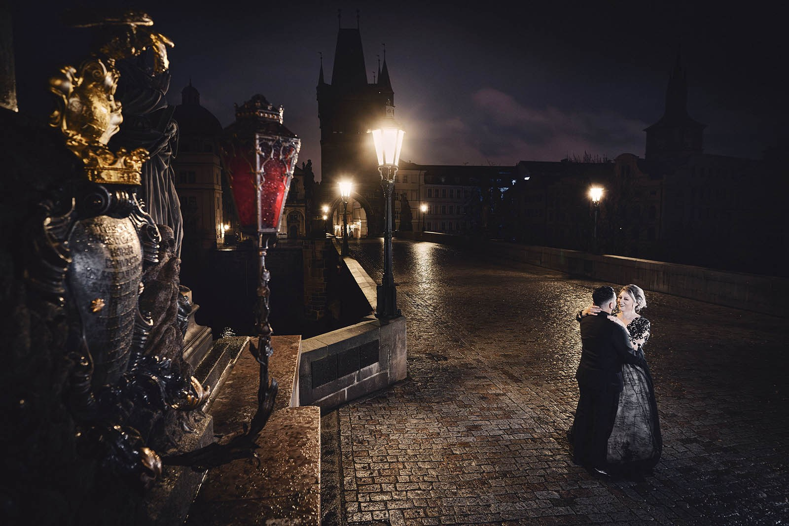 Couple in black dancing embracing under the Cavalry statue atop Charles Bridge at night