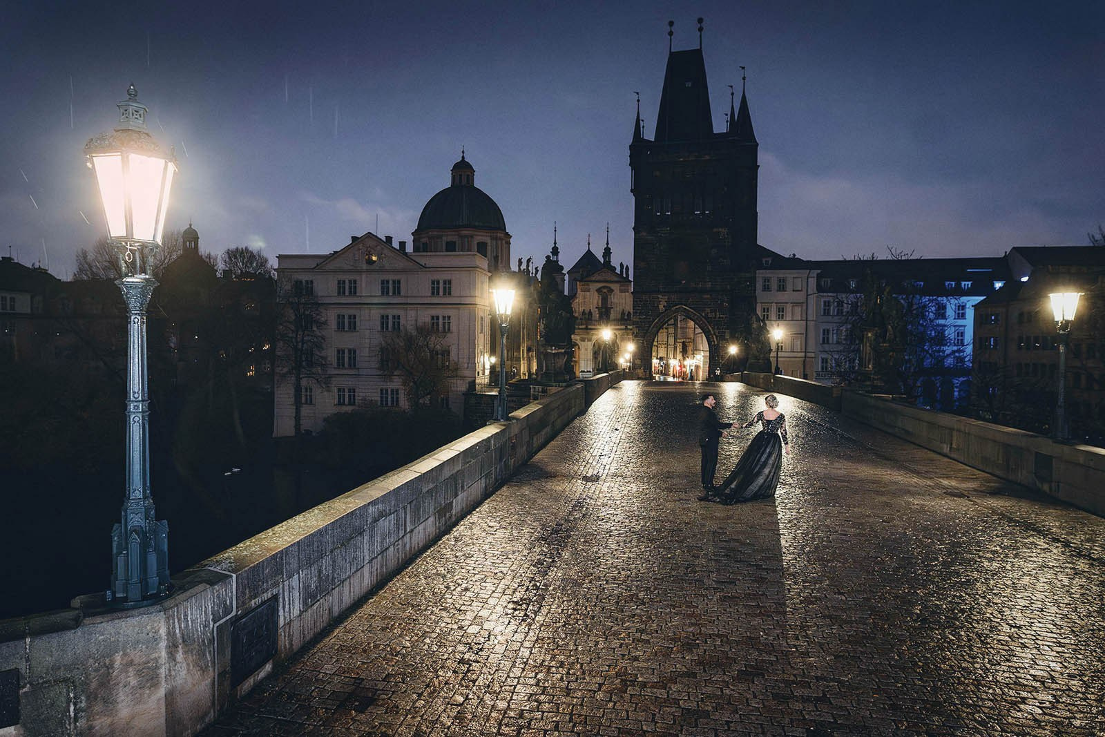 Couple dancing on the wet Charles Bridge at night in the rain, iconic Prague gothic anniversary session  