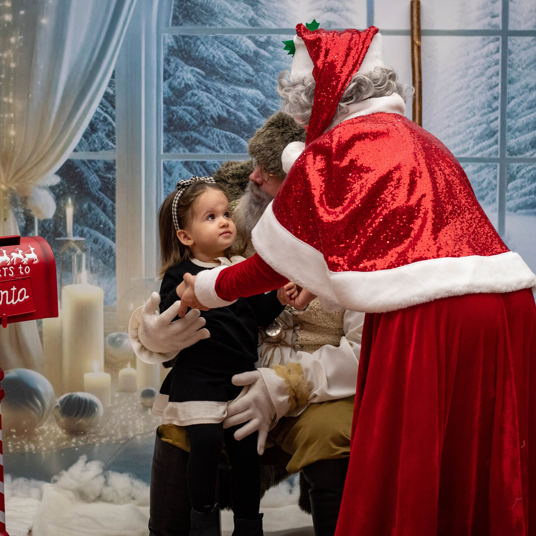 Santa Claus handing a gift to a child at a festive Christmas setup indoors.